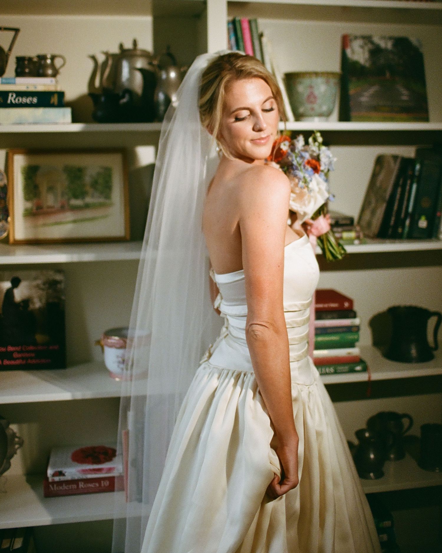 A wedding dress is showcased in a room with built-in bookshelves and natural lighting.