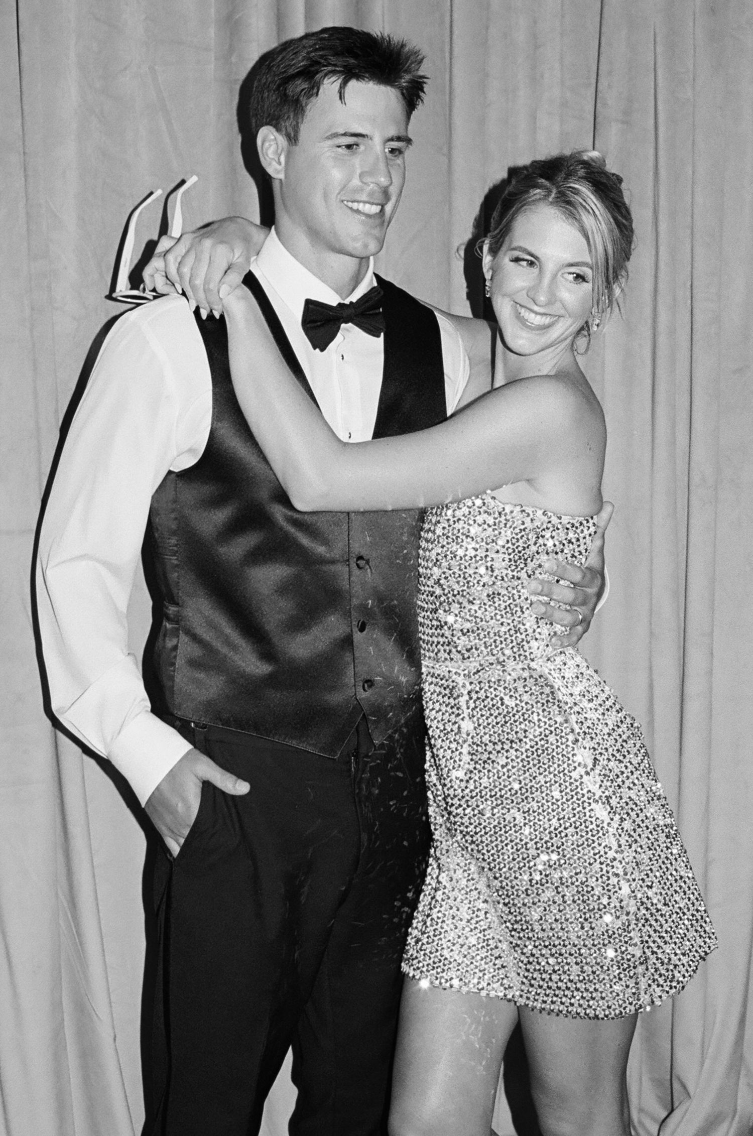 Formal event with couple in evening attire posing against light backdrop.