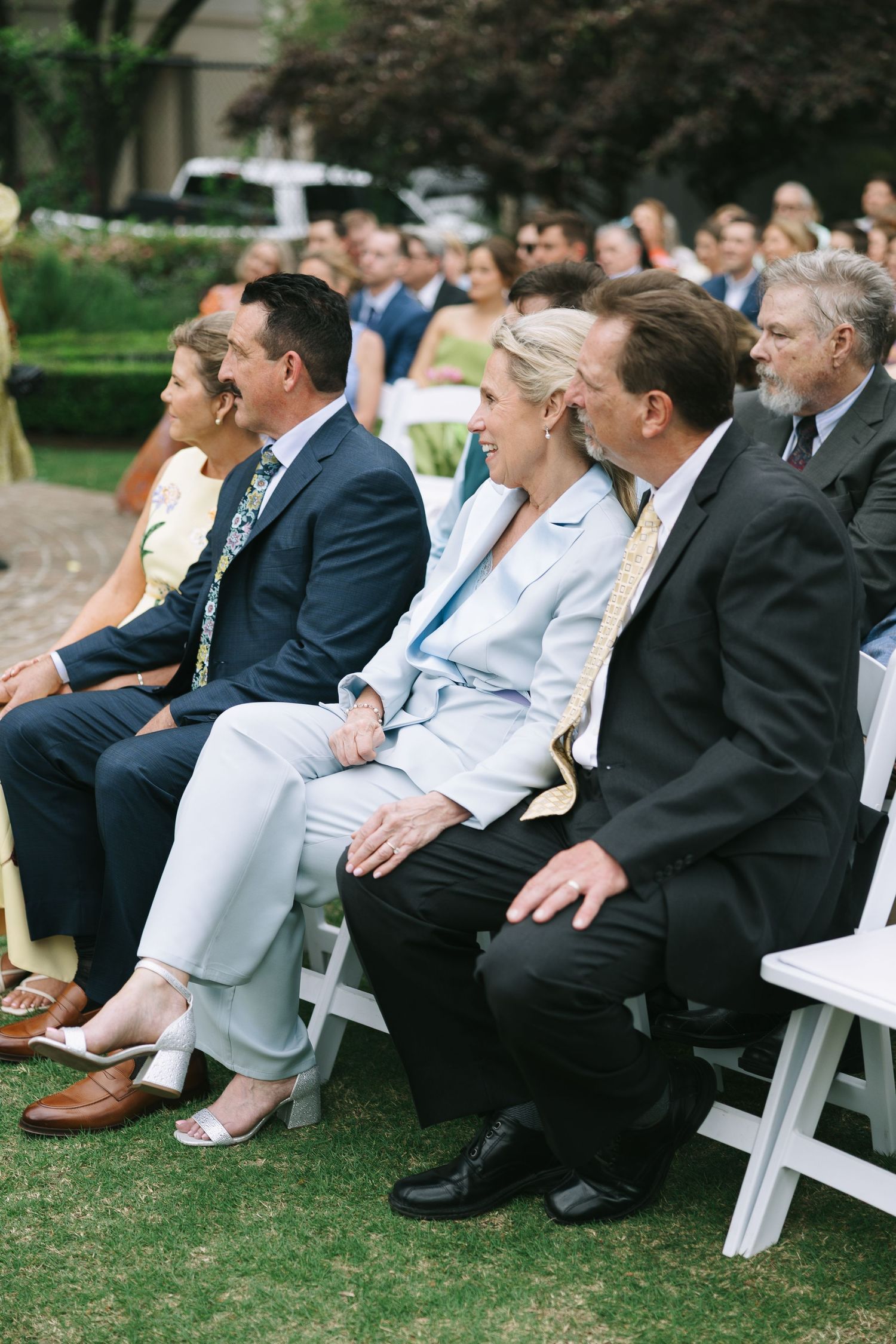Wedding guests seated in white chairs on a lawn during an outdoor ceremony.