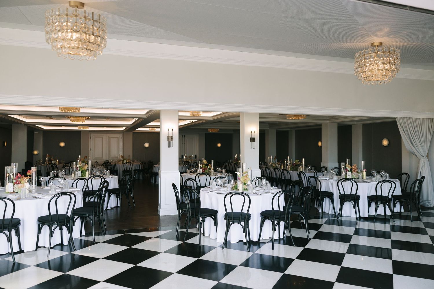 Spacious ballroom with black and white checkered floor and crystal chandeliers.