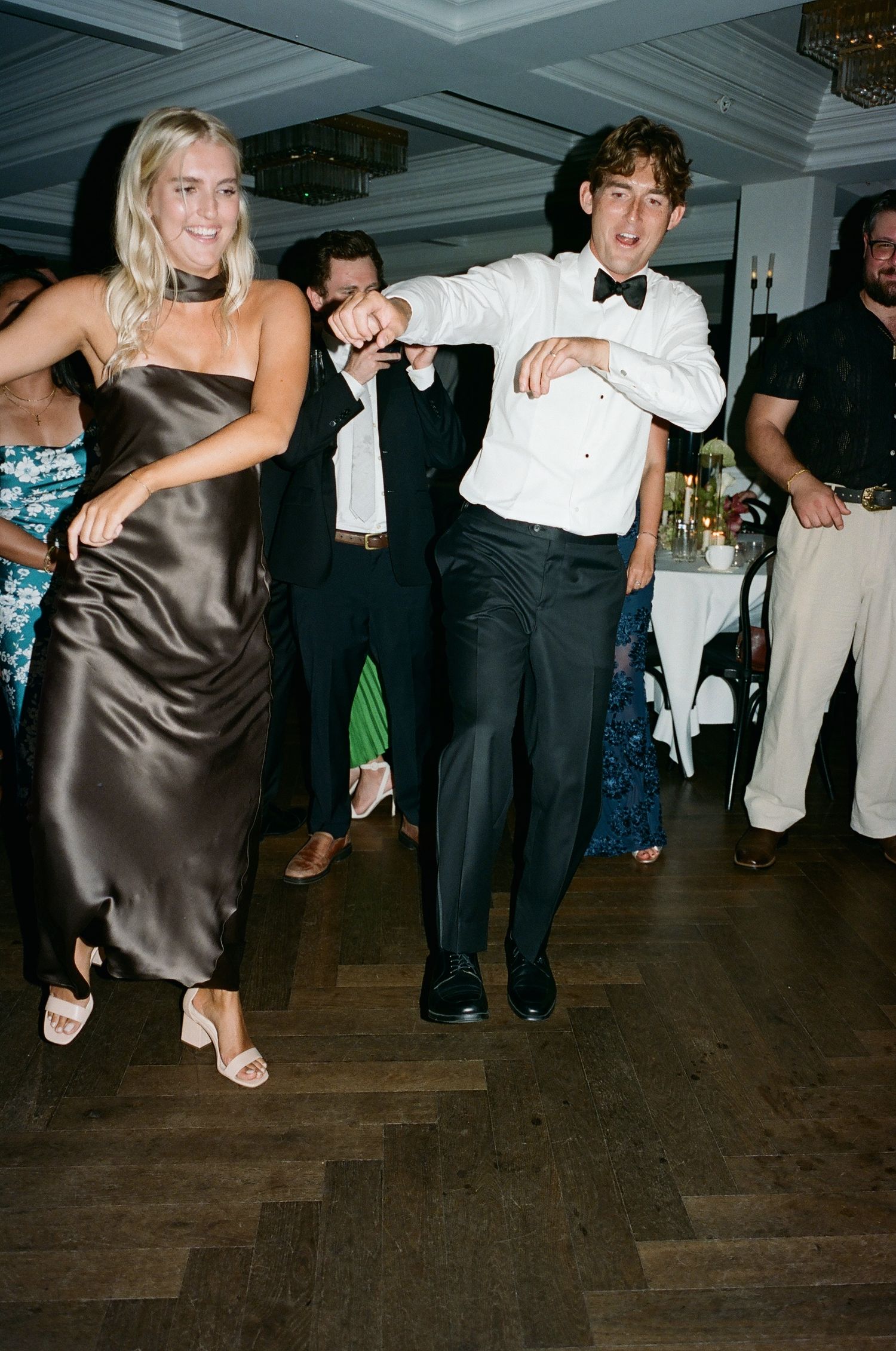 People dancing in formal attire on a dark wooden floor at an evening event.