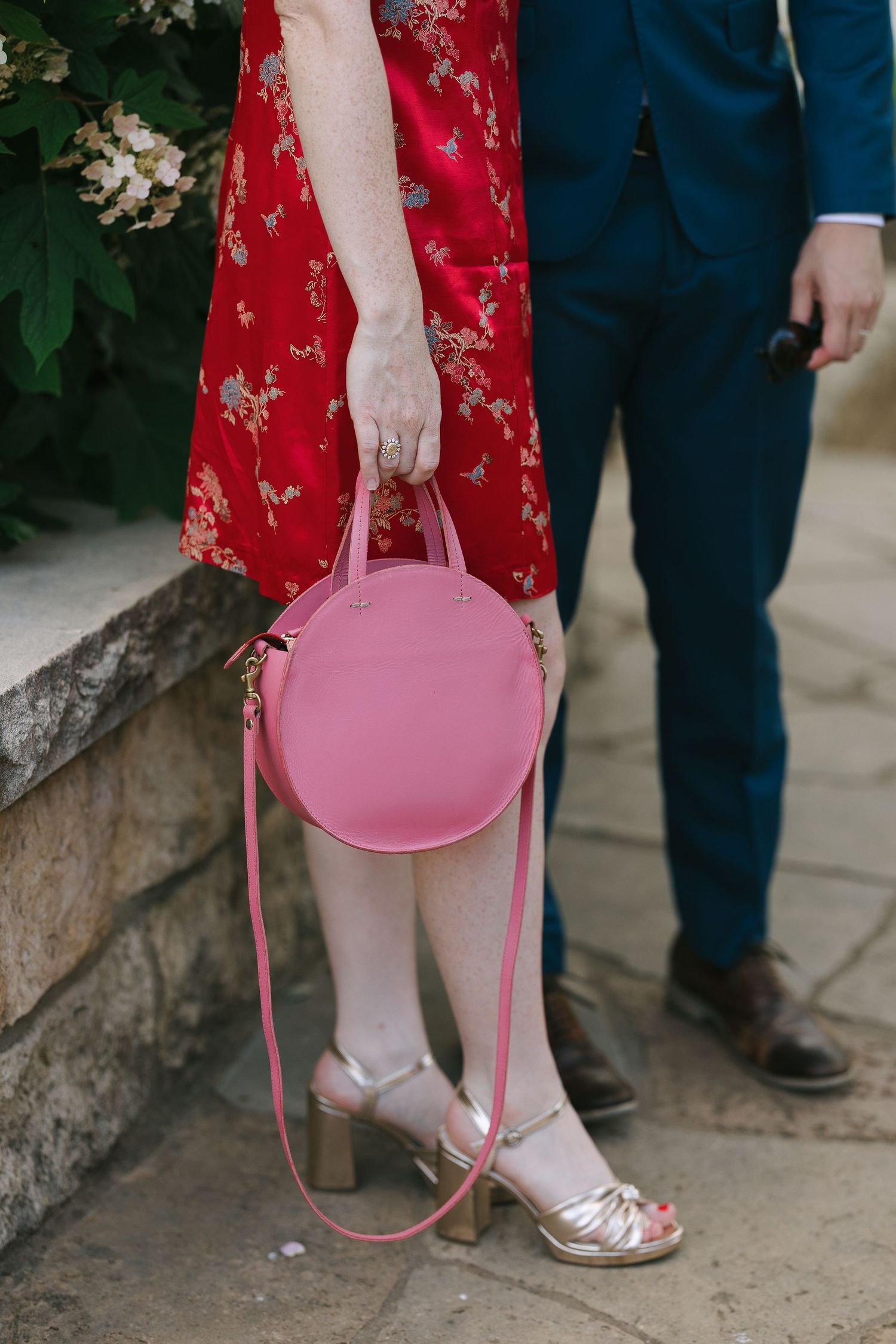 Close-up of a person in a red dress carrying a pink handbag with metallic sandals.
