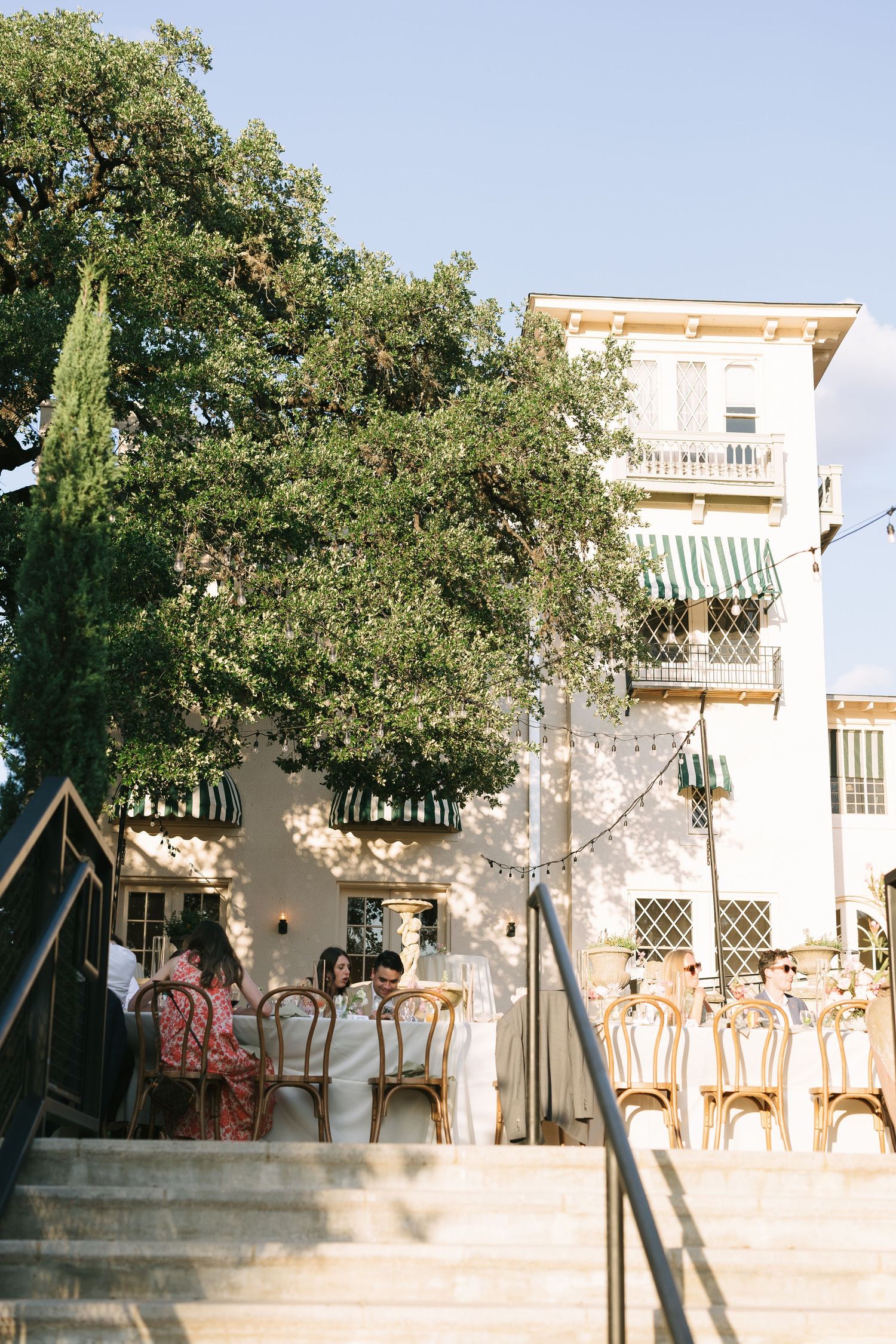 Elegant white building with balconies and trees against a bright blue sky.