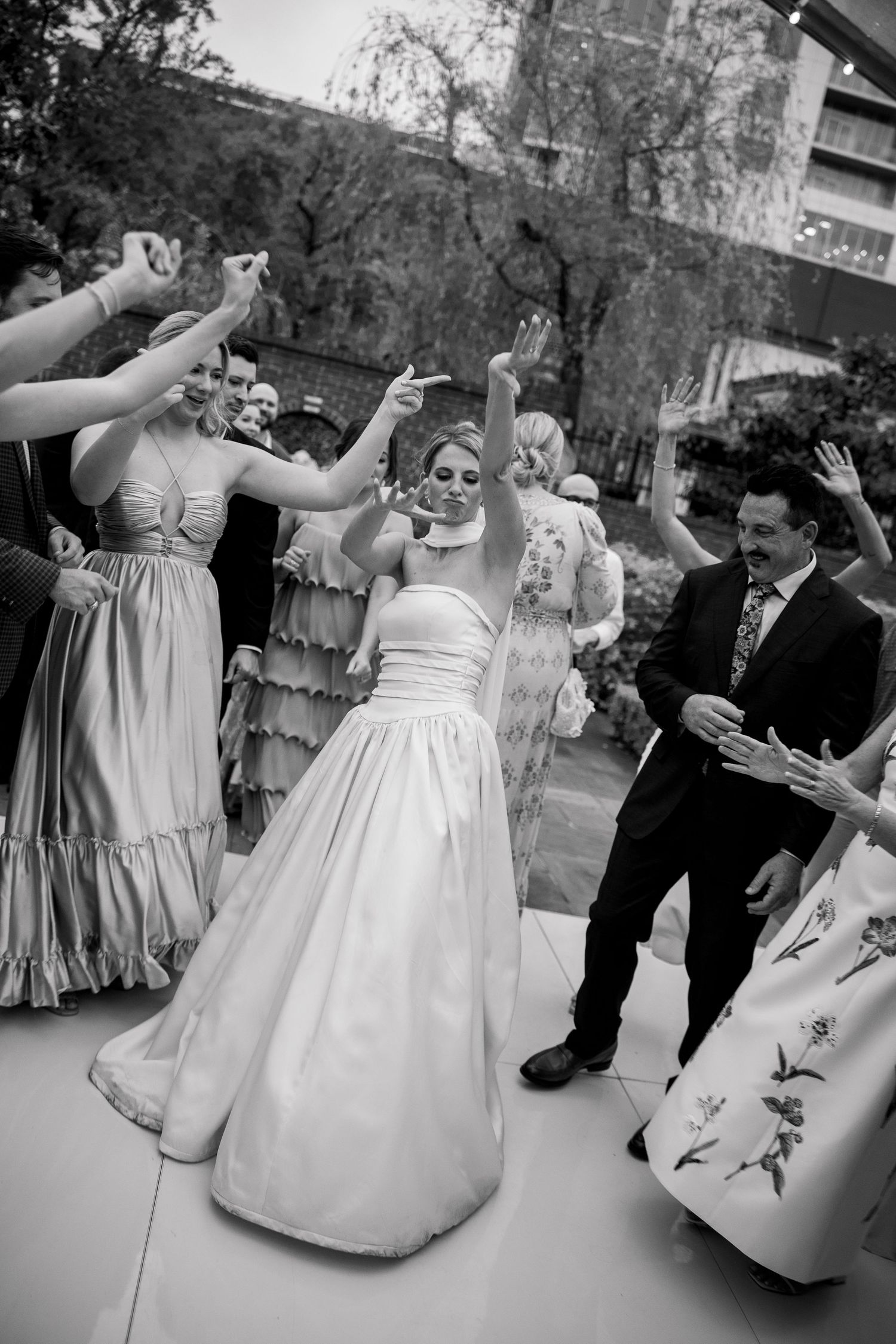 Wedding party dances in a circle on an outdoor dance floor.