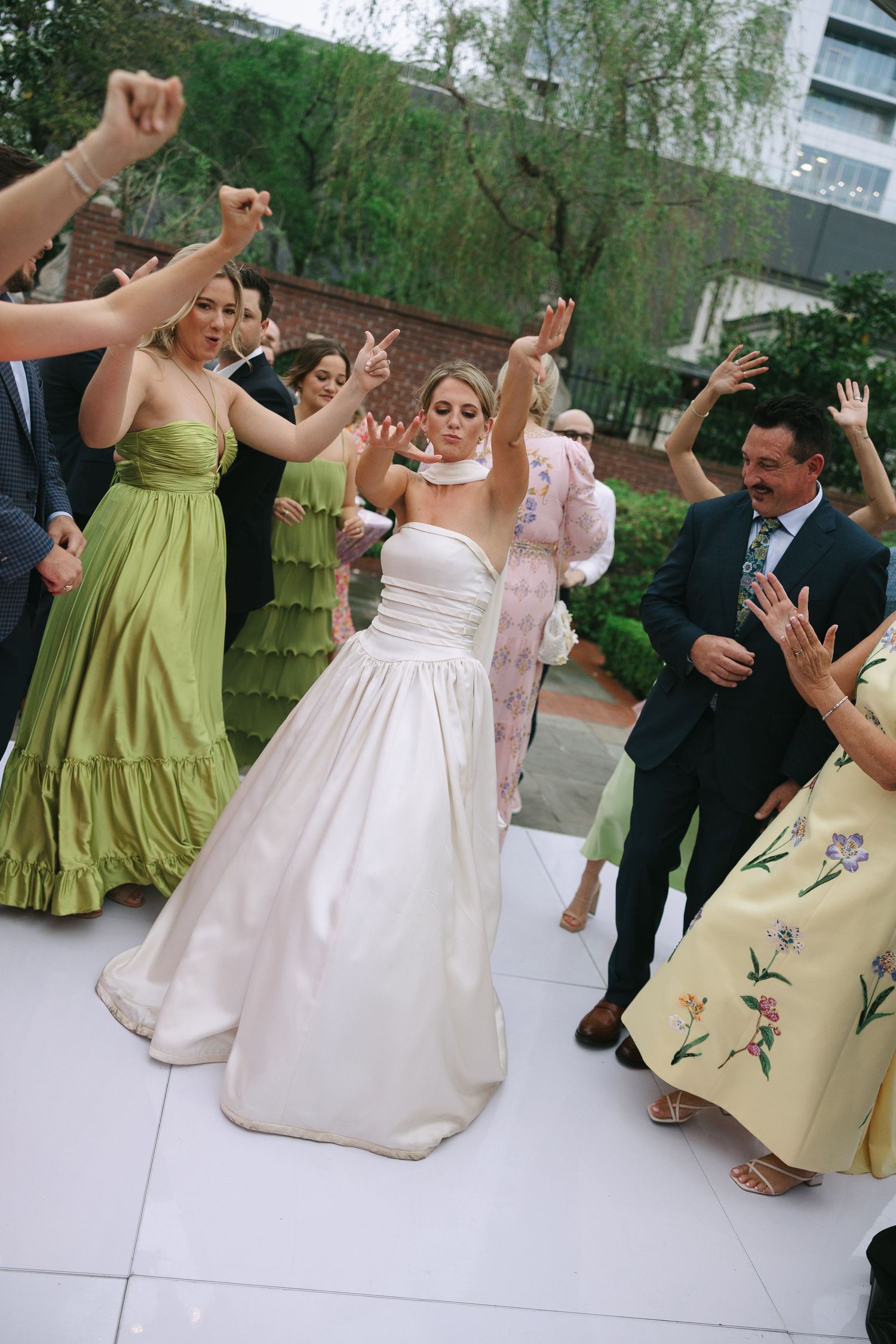 Wedding celebration with dancers in green bridesmaid dresses and white gown on outdoor dance floor.