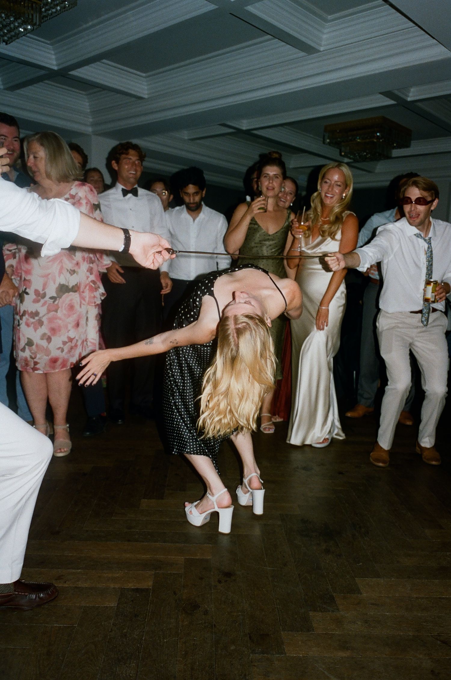 Party guests dance energetically on a wooden dance floor during a celebration.