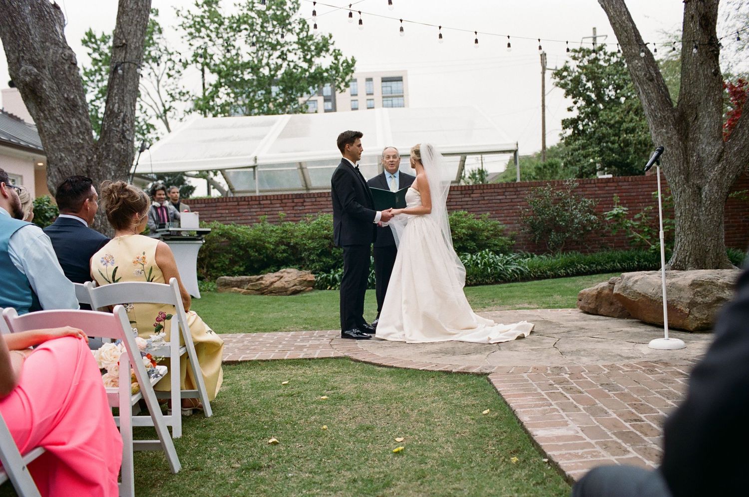 Couple exchanges vows during outdoor garden wedding ceremony with guests watching.