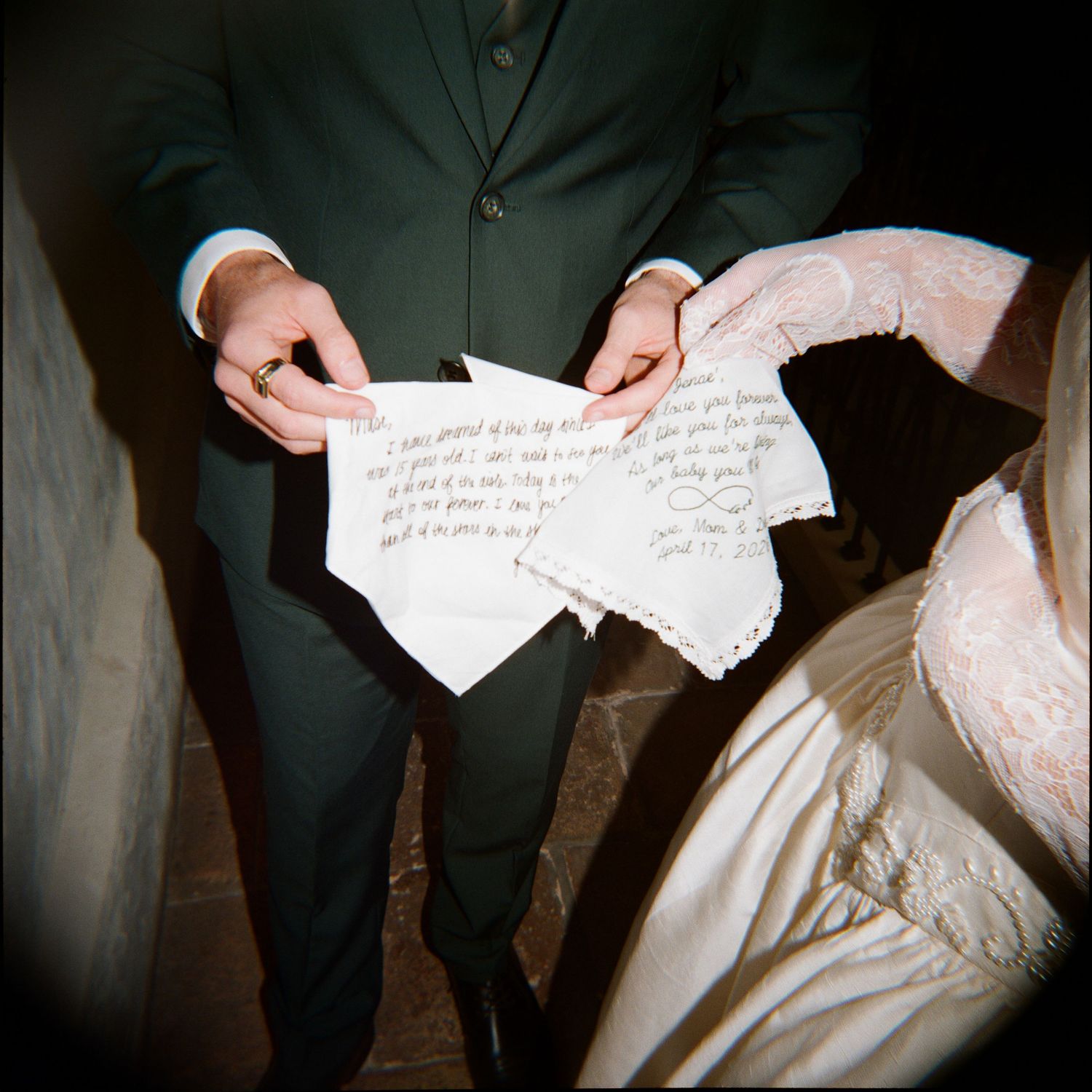 Bride and groom holding handwritten wedding vows on torn paper, wearing formal attire with lace dress detail.