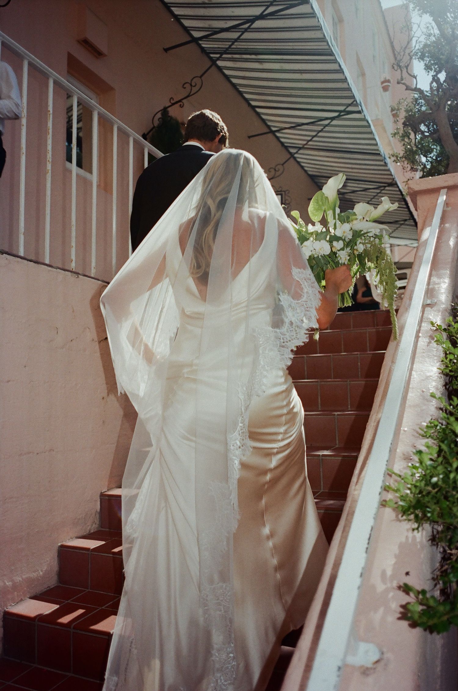 A white wedding dress hangs elegantly against a pink wall with natural lighting.