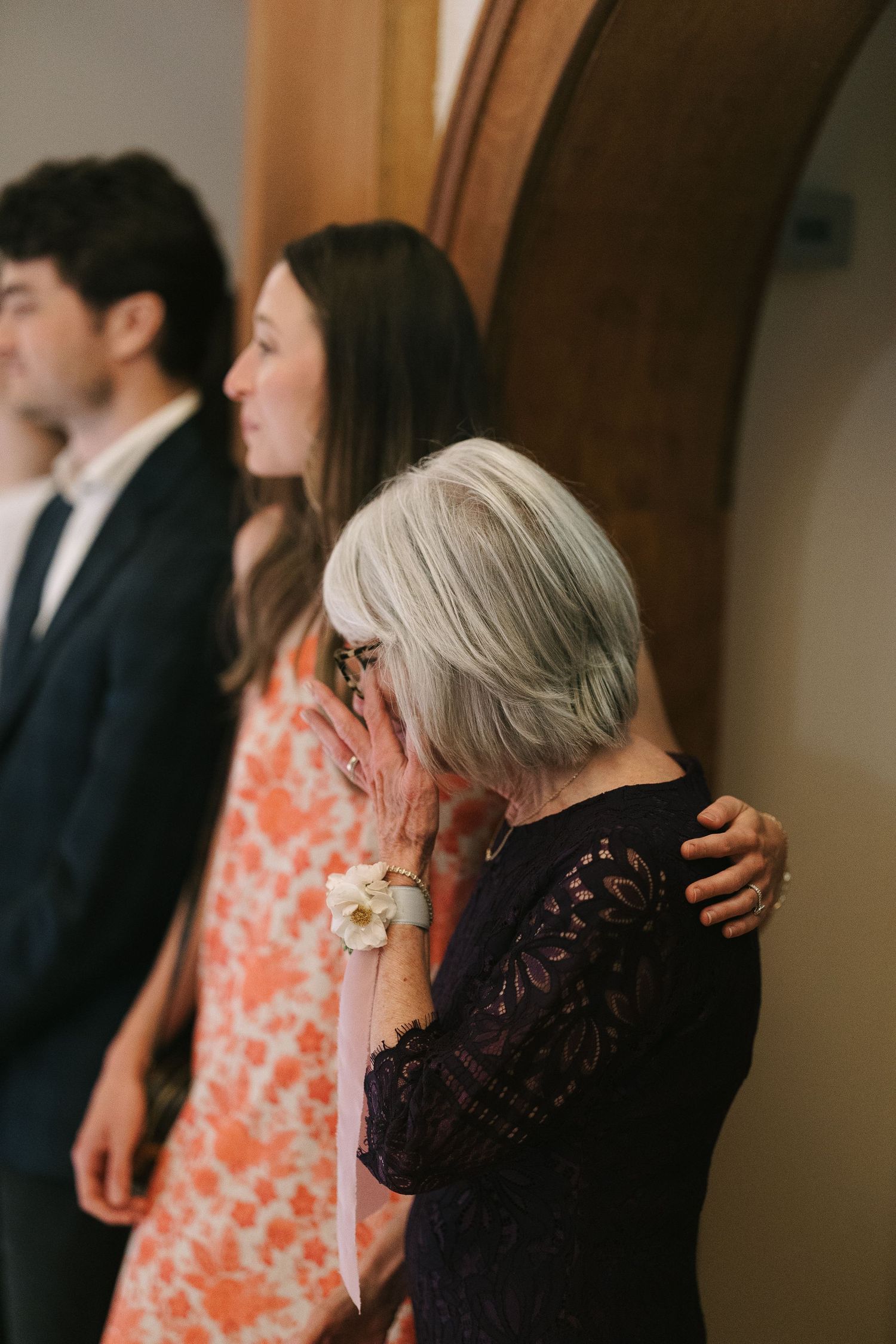 Two people share an emotional moment at a formal event, one wearing black lace and another in a coral dress.
