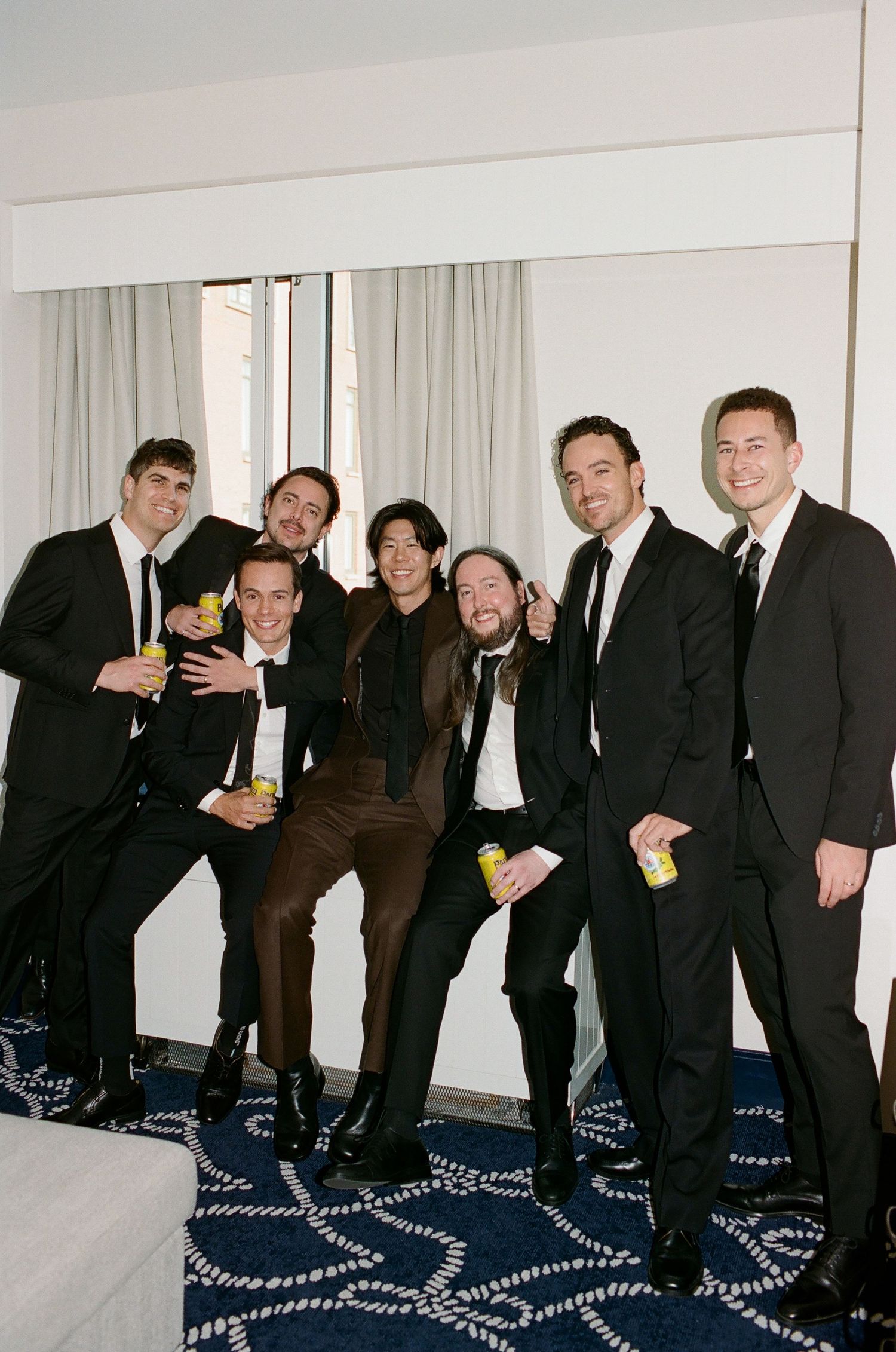 A group of formally dressed people in suits lean and pose together in a sequence of four connected photos.