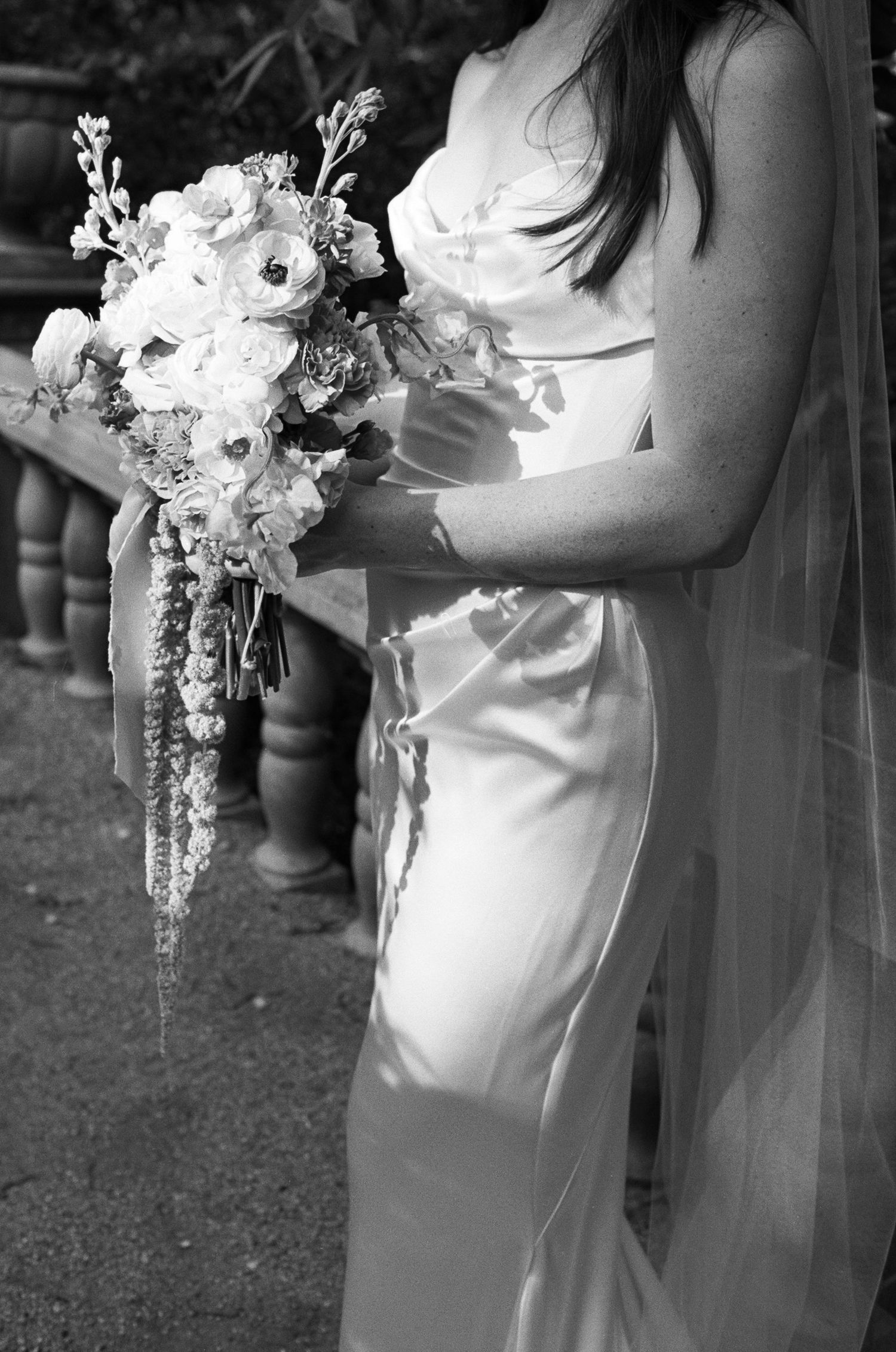 Close-up details of a bride's white wedding dress and cascading floral bouquet.