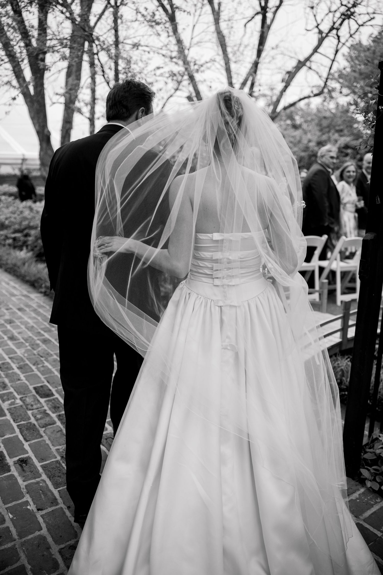 Detail shot of a white wedding dress with flowing veil against brick pavement.