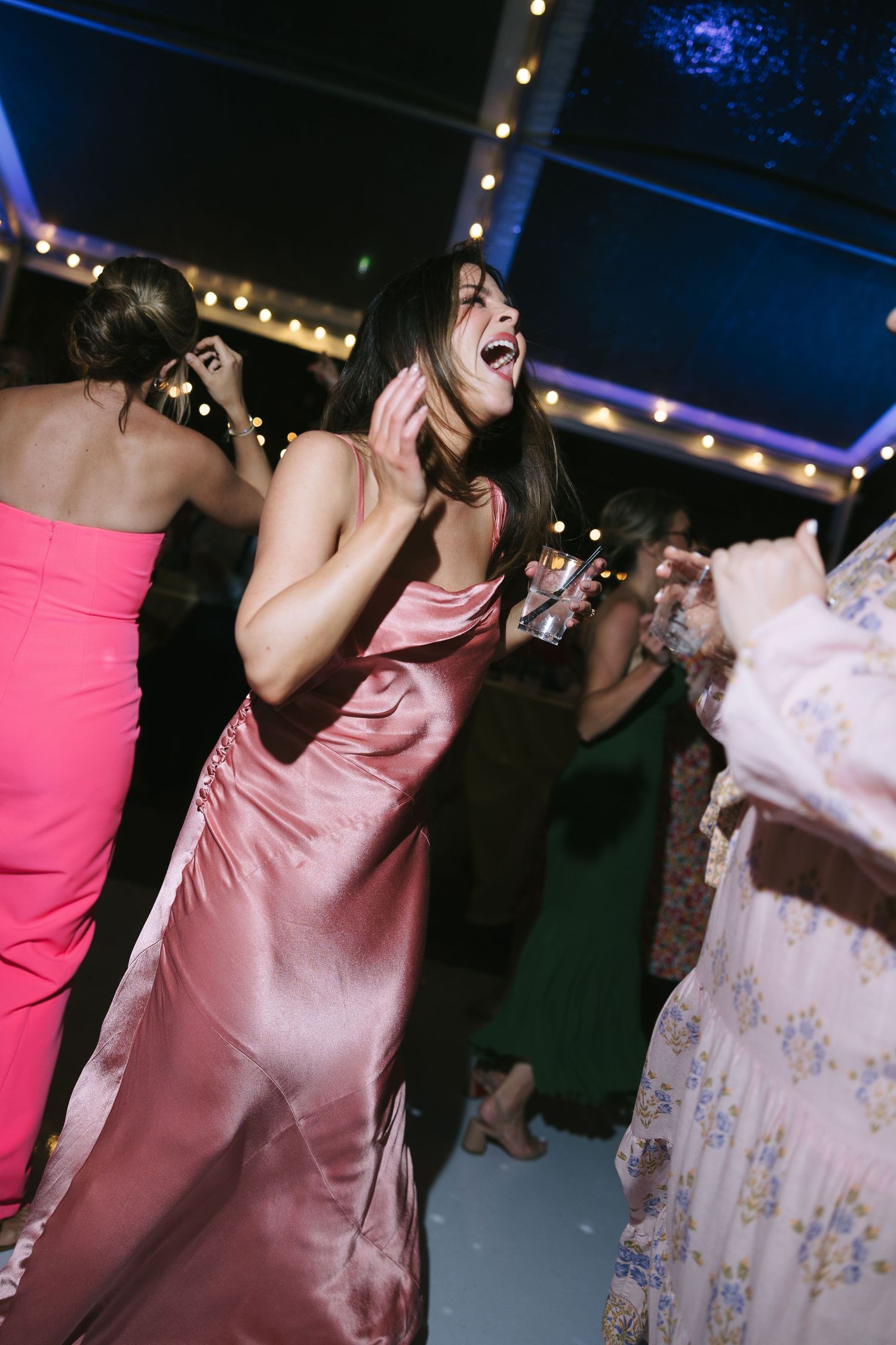 Wedding guests in pink and floral dresses dancing enthusiastically at a nighttime reception.