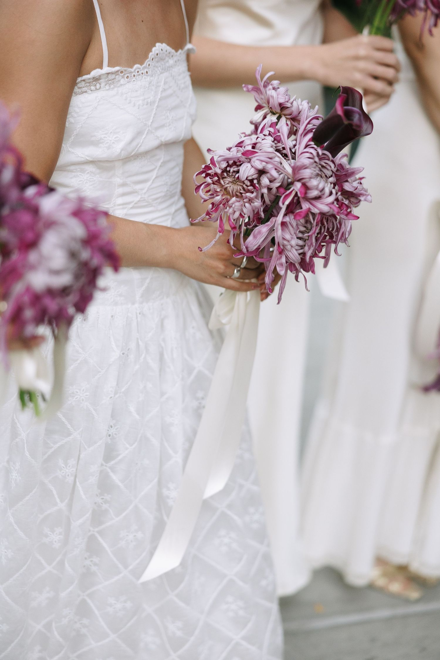 Detail shot of white lace wedding dresses with purple bouquets held at waist level.