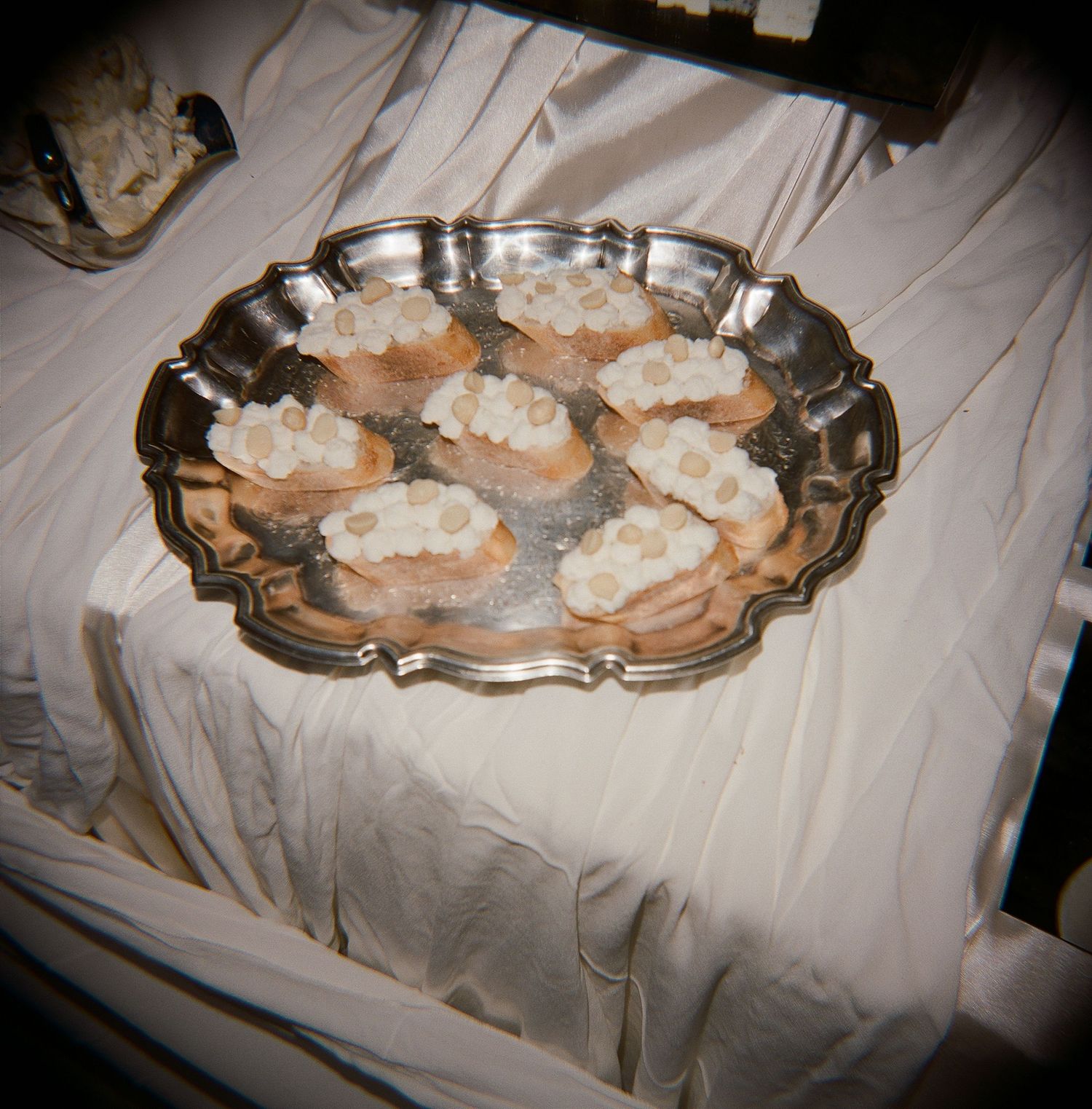 Silver decorative tray with bruschetta topped with cream cheese and banana slices on a white tablecloth.
