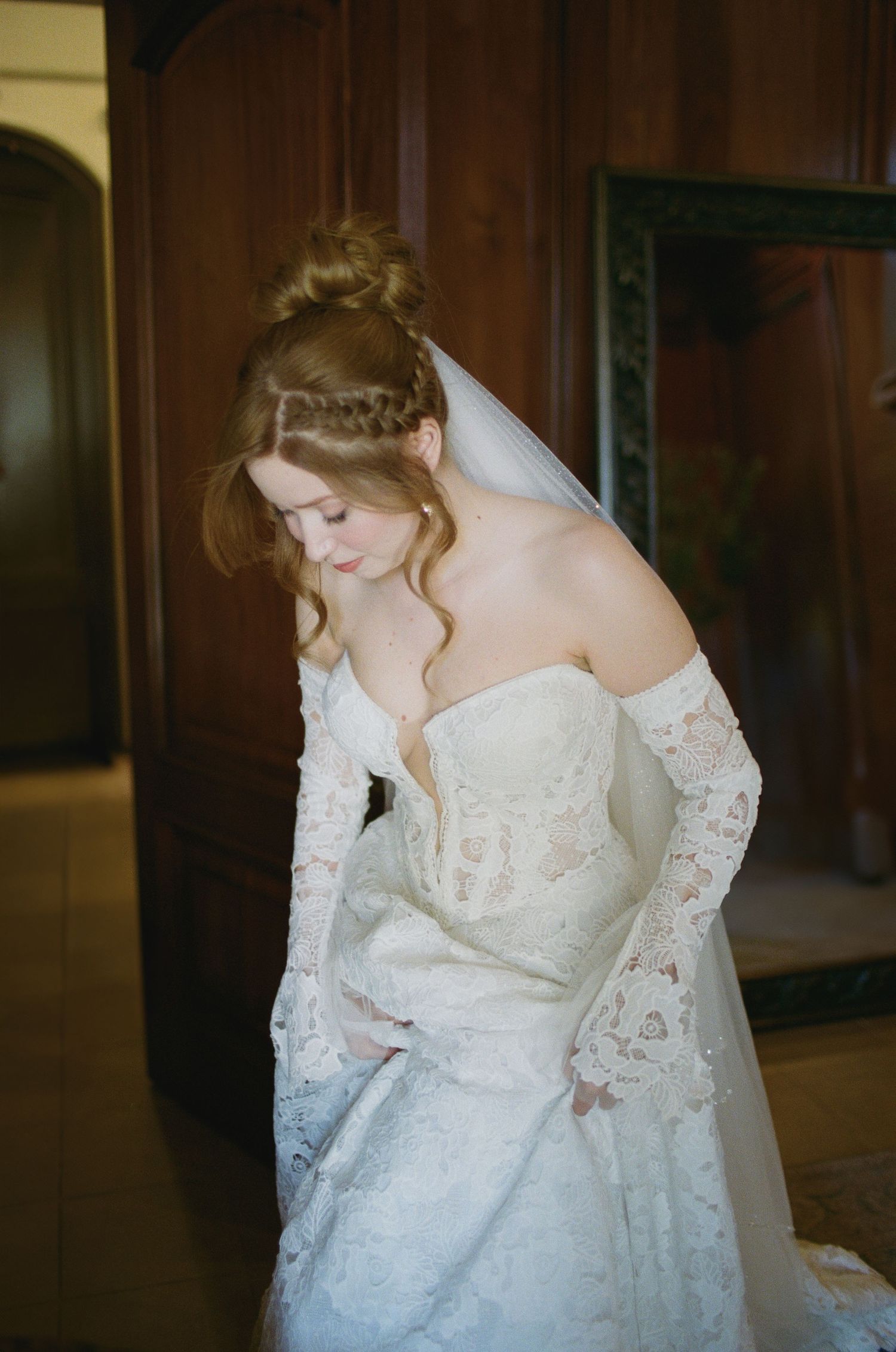 A bride in a delicate lace wedding gown with long sleeves poses elegantly in a romantic setting.