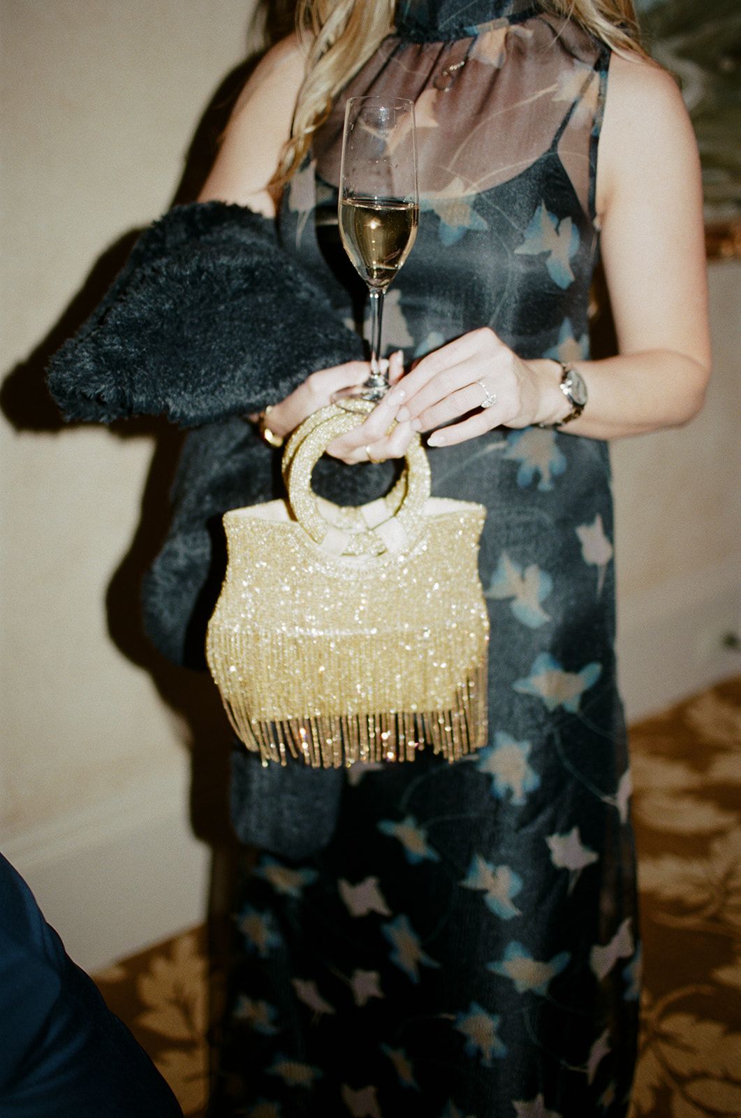 Person holding a champagne glass next to a sparkly gold evening clutch.