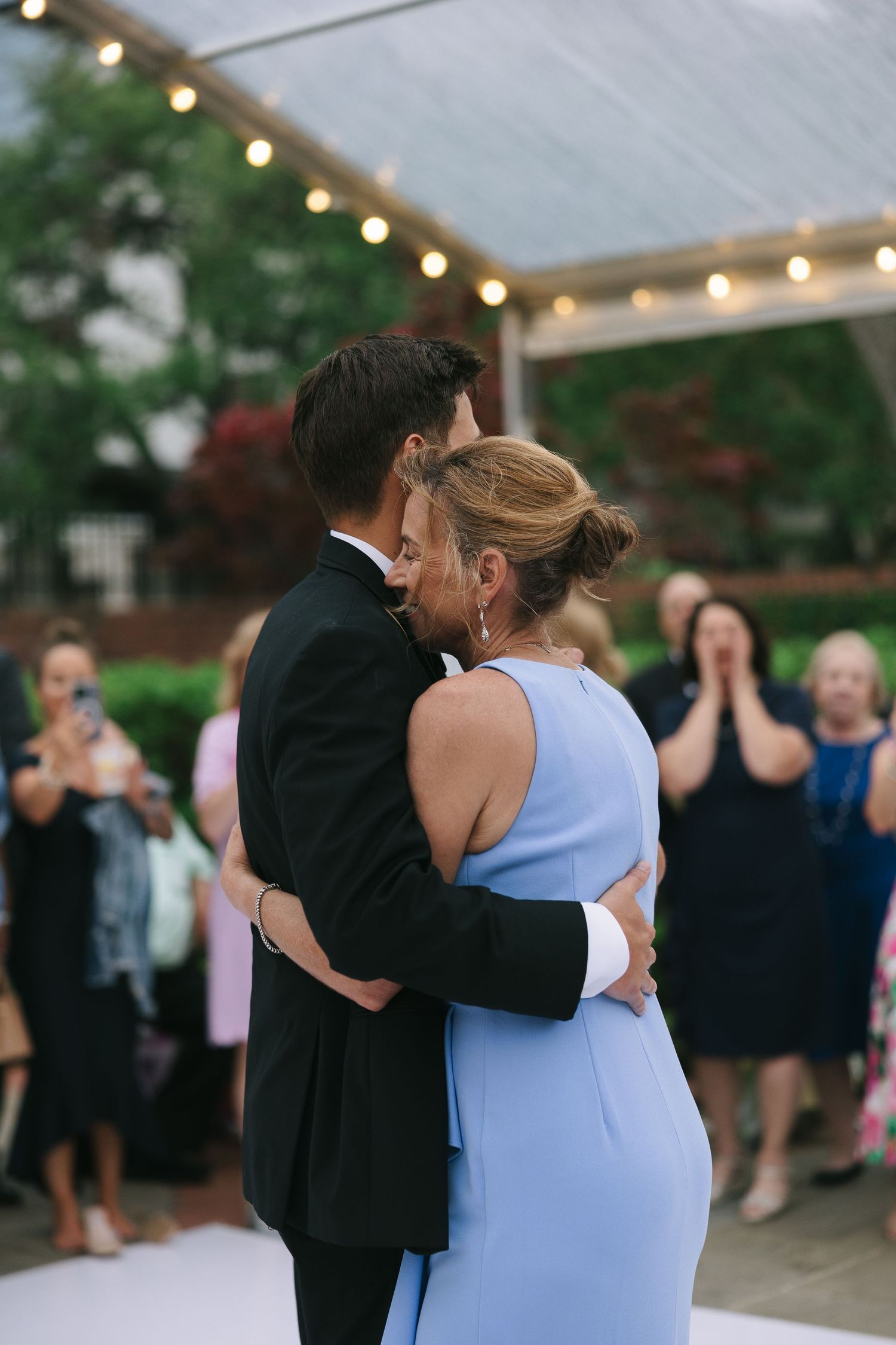 A couple dances closely while wedding guests look on at an outdoor reception.