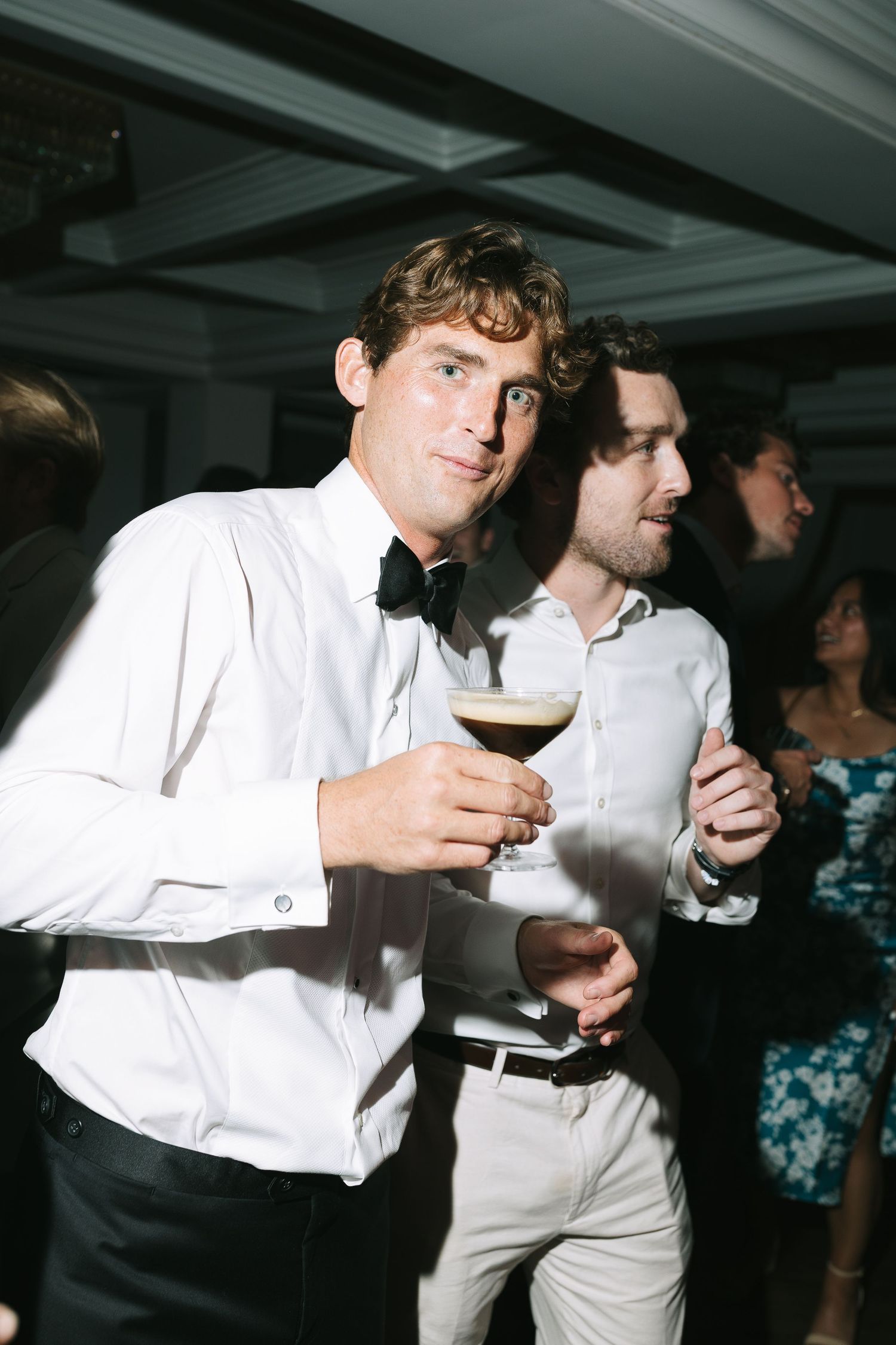 People in formal attire enjoying drinks and dancing at an indoor reception.