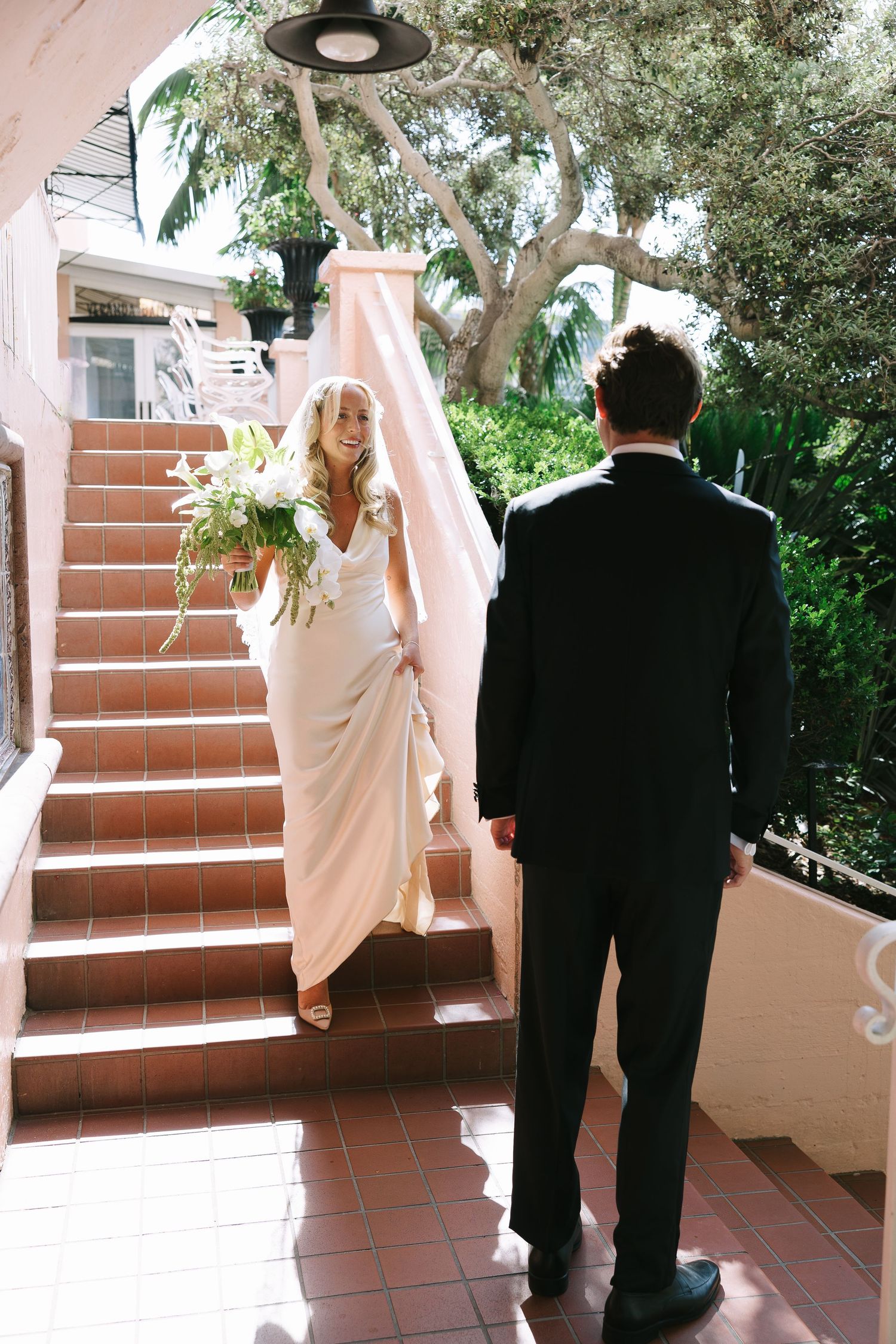 A formal wedding scene on terracotta steps with flowing white fabric and natural greenery.