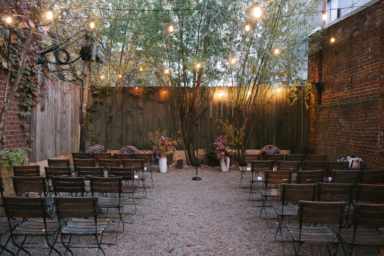 String lights illuminate a rustic outdoor patio area with metal chairs and brick walls creating an intimate ambiance.