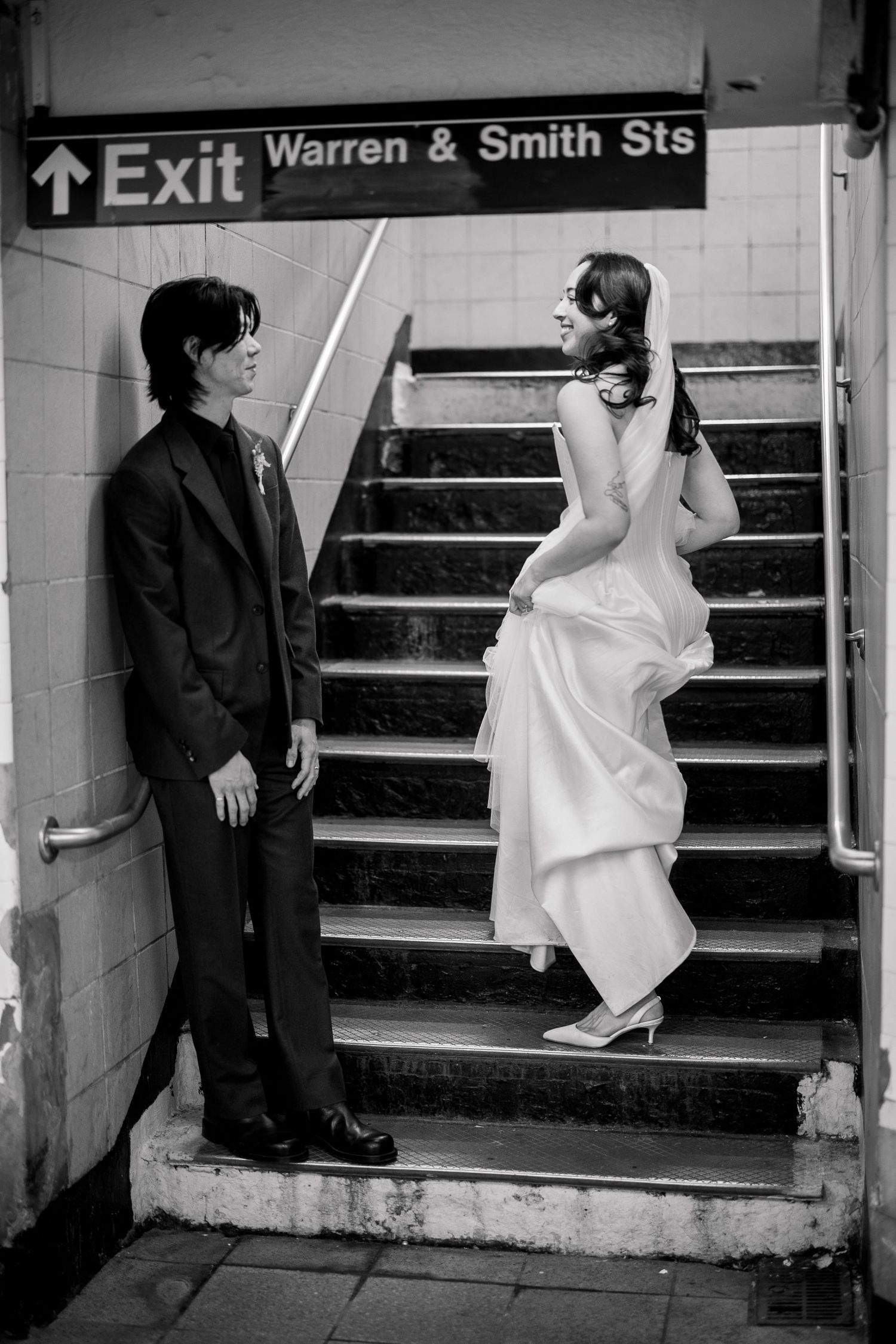 Couple in wedding attire poses on subway station stairs near Warren & Smith Streets exit sign.