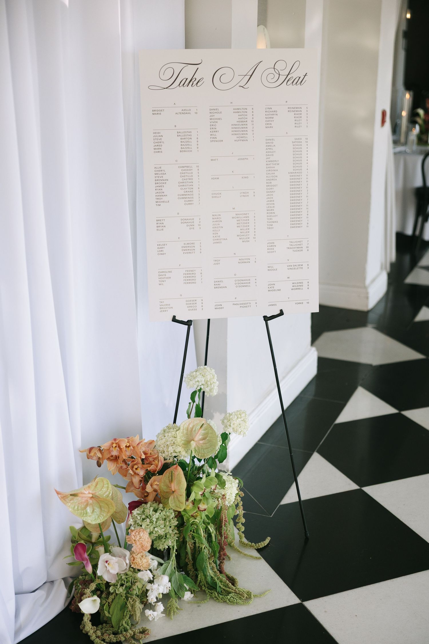 Wedding seating chart display with floral arrangements and white draping.