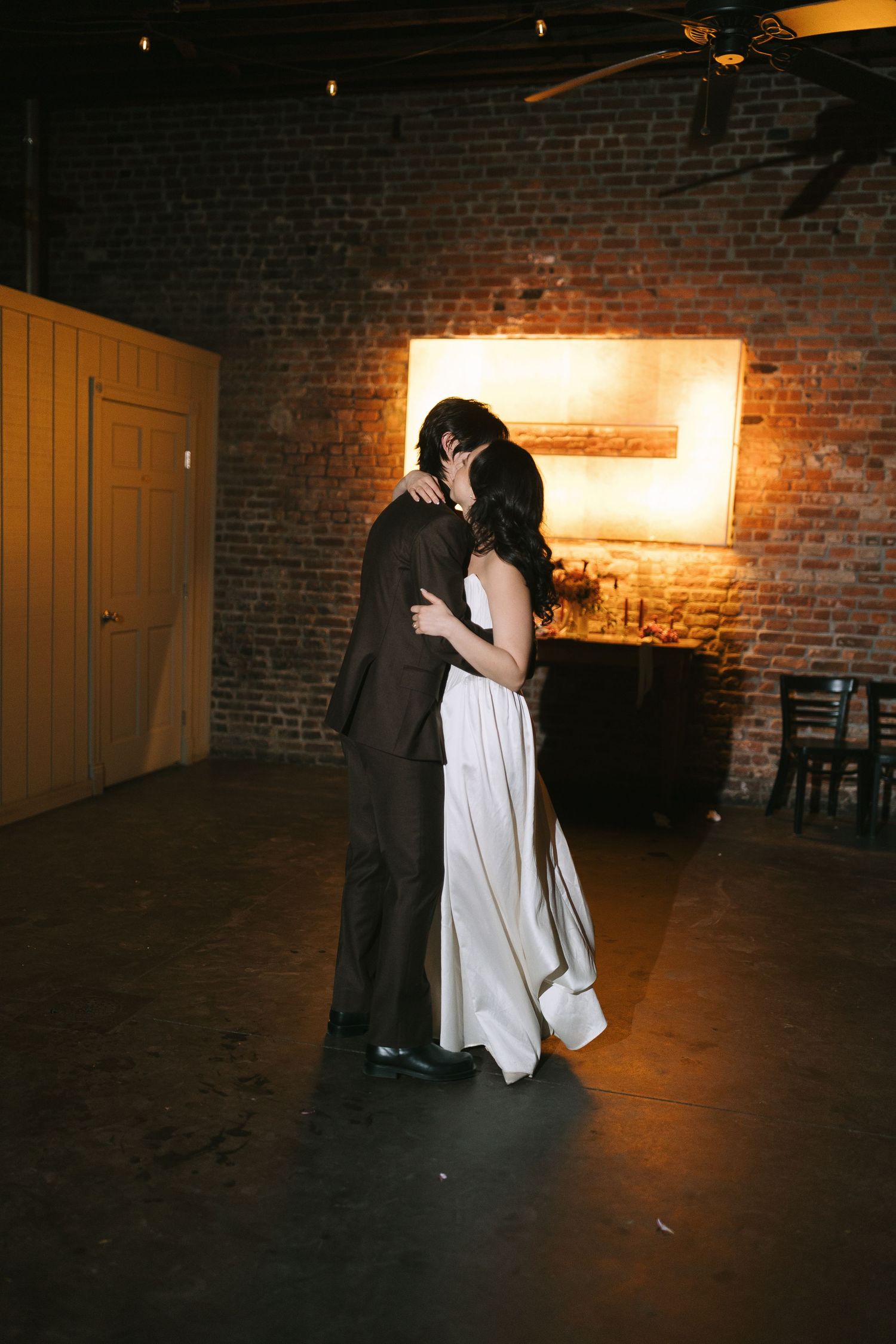 Romantic dance moment captured in dimly lit brick venue with warm glow.