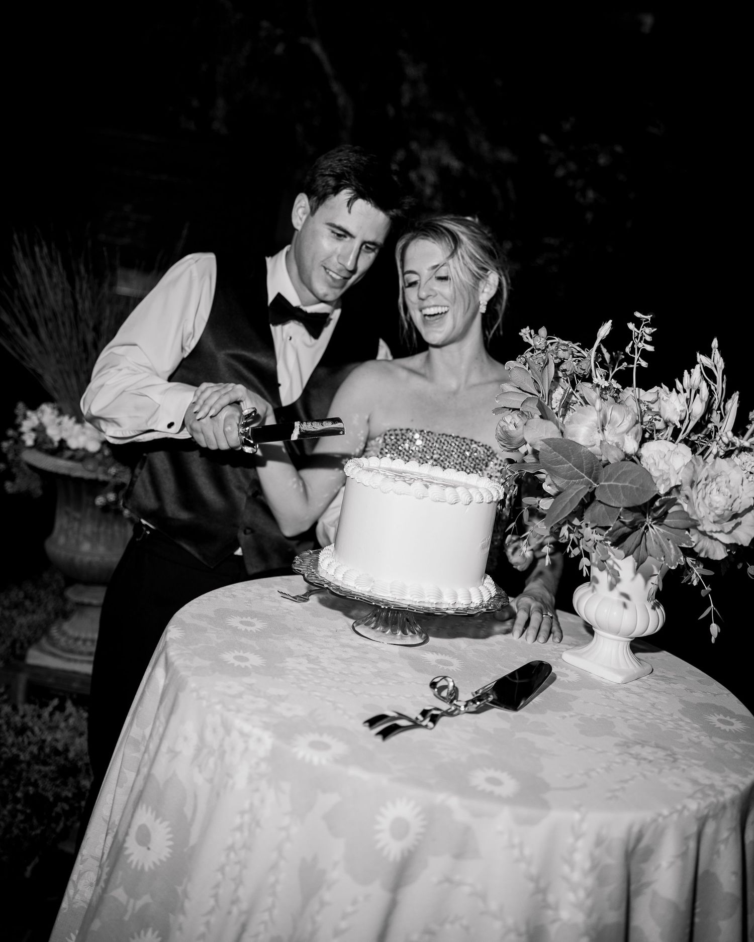 Couple sharing their wedding cake at an outdoor reception with floral decorations.