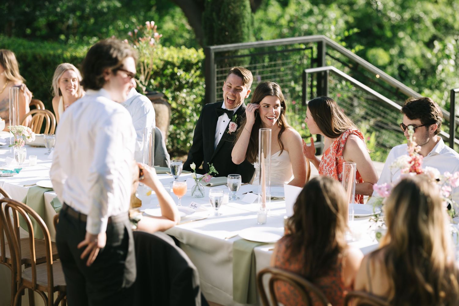 Outdoor wedding reception with guests mingling at decorated tables under natural lighting.