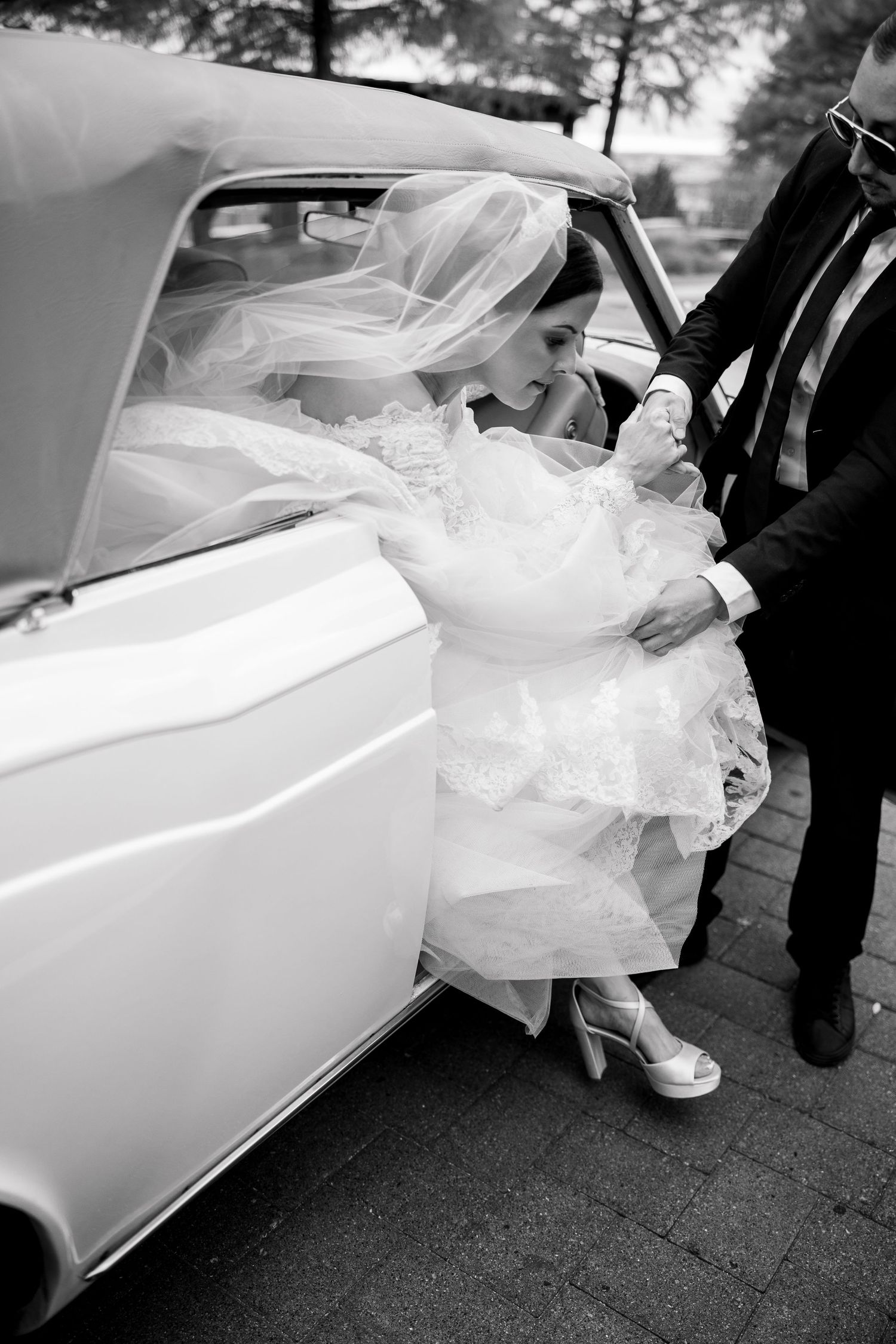 Black and white photos of a bride's dress being arranged as she enters a classic white car.