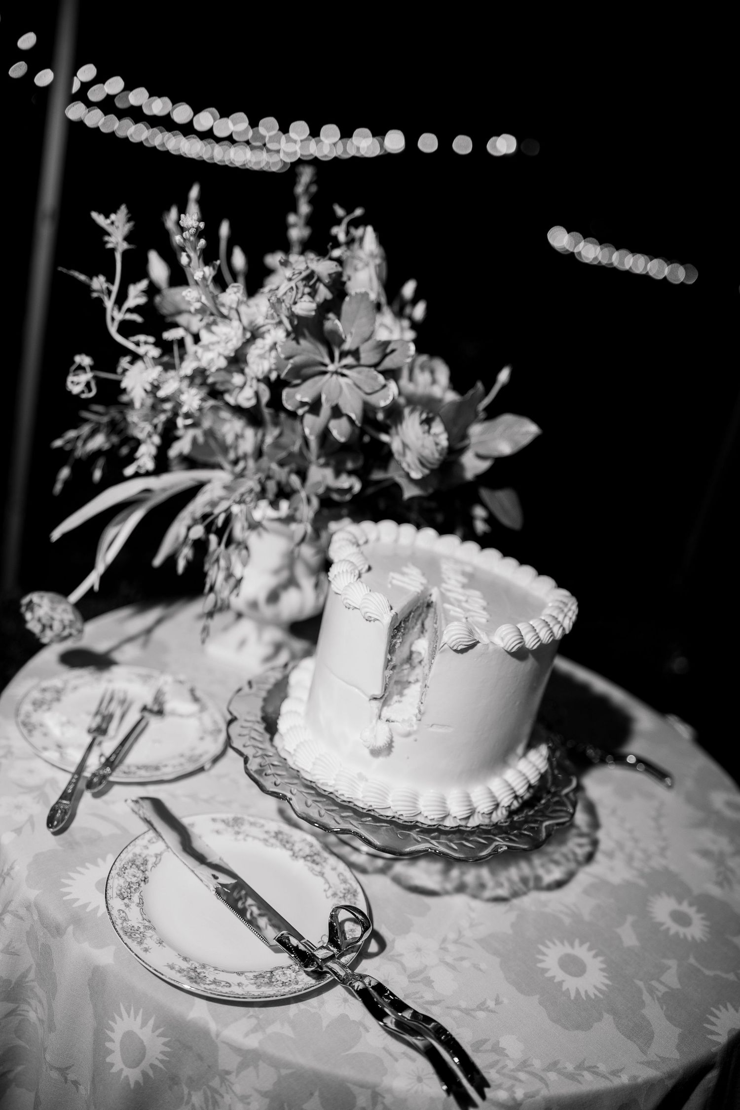 Elegant white wedding cake with floral decorations on a patterned tablecloth.