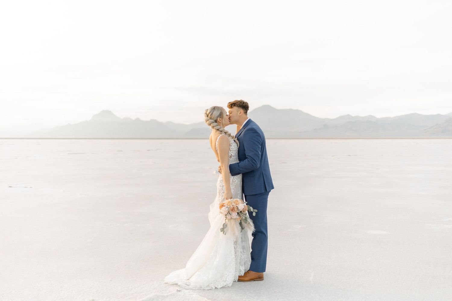 Newlyweds share an intimate moment while posing in front of mountains on their wedding day at Salt Flats, Utah
