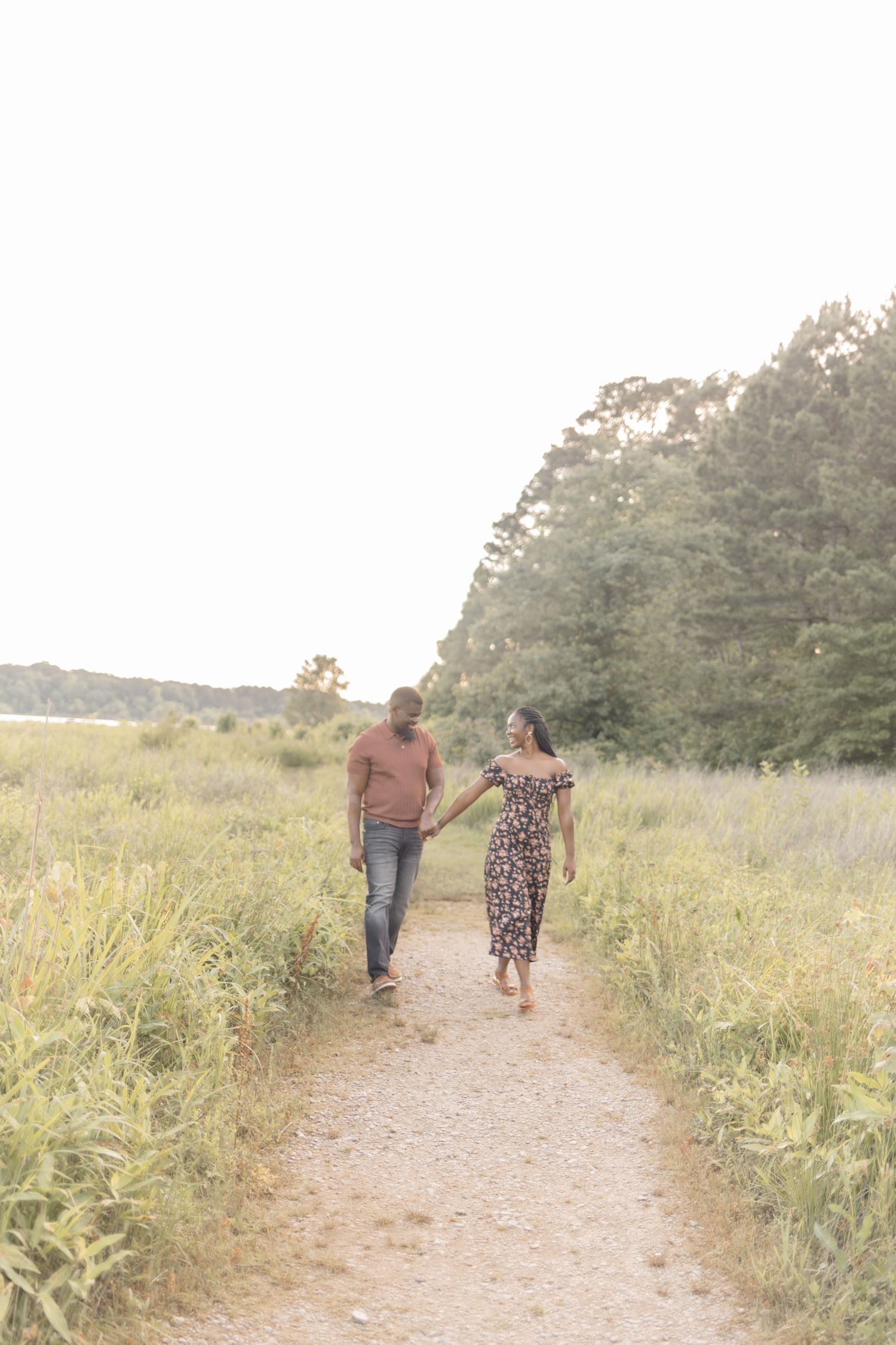 Couple holding hands walking on a scenic path surrounded by lush greenery during golden hour.