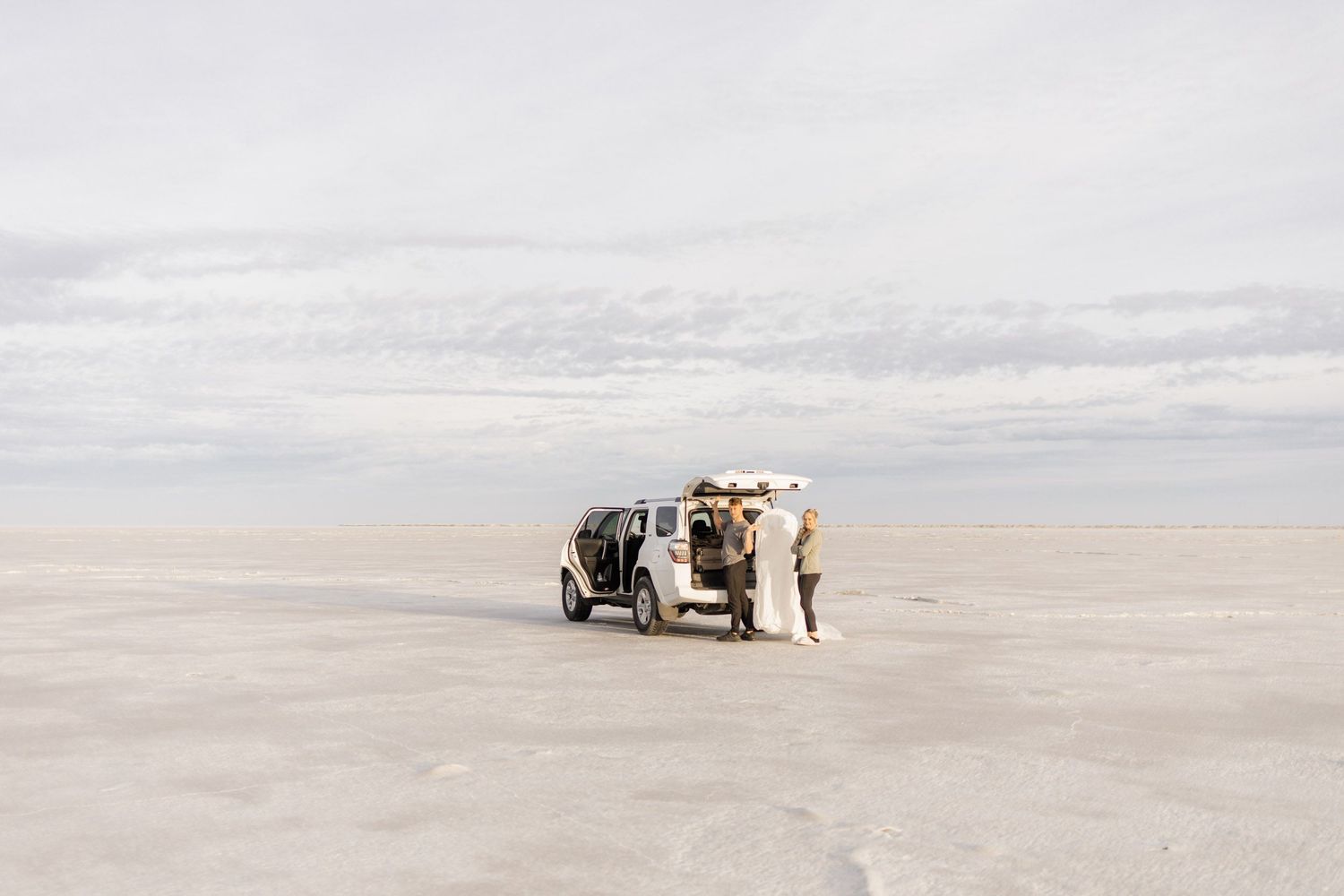 A vehicle parked on the expansive salt flats with people taking photographs in the distance.