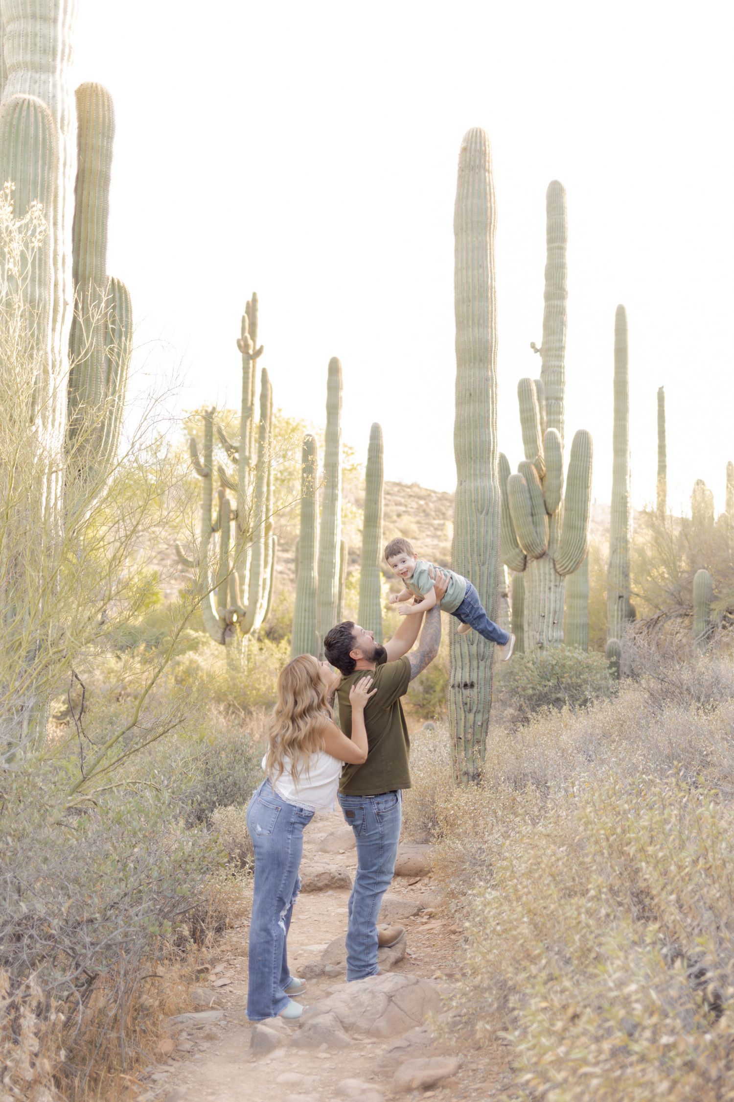 A couple lifts their toddler among towering saguaro cacti on a desert trail in Arizona.