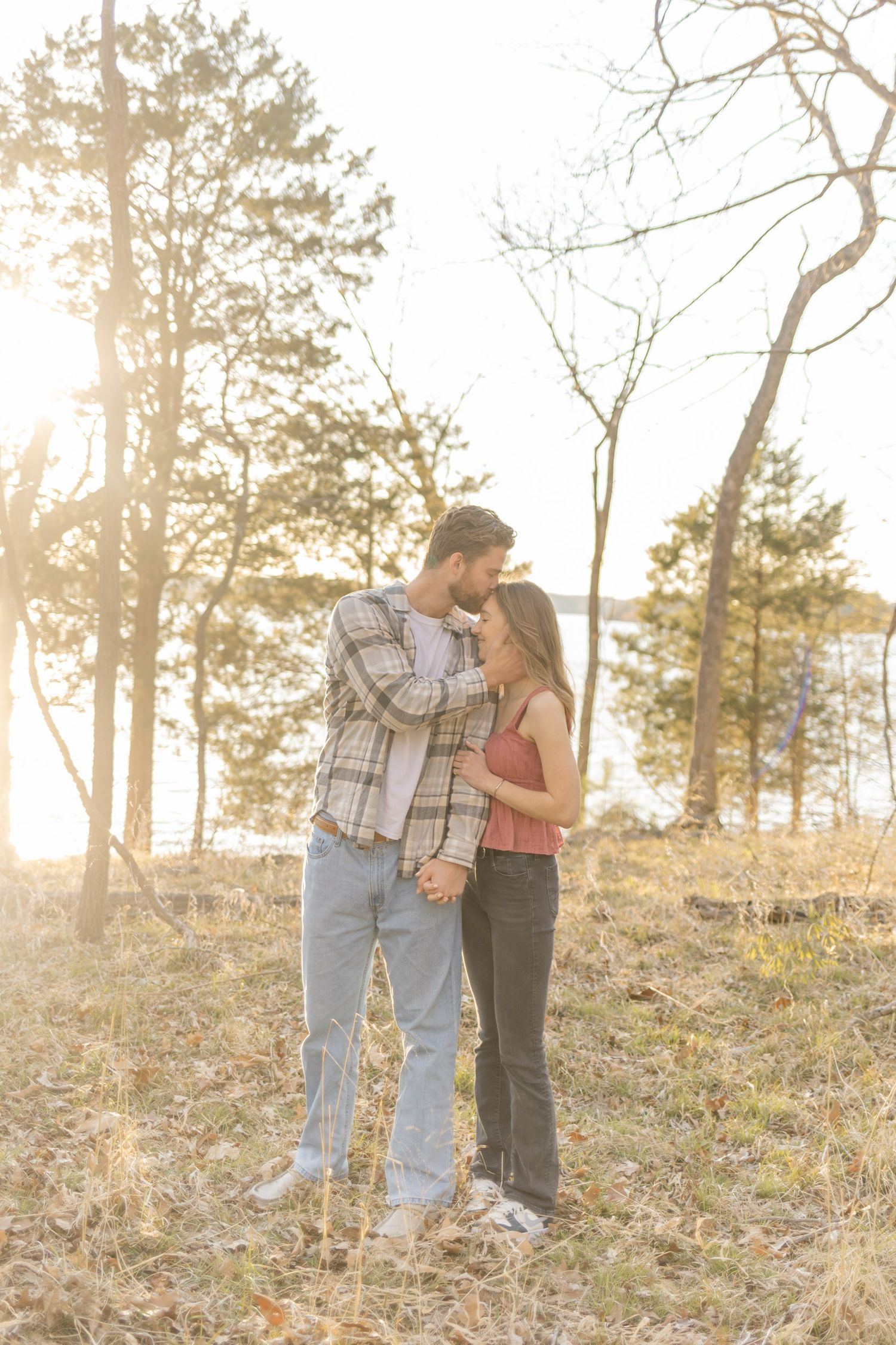 Couple walking together on a hillside with pine trees during golden hour.