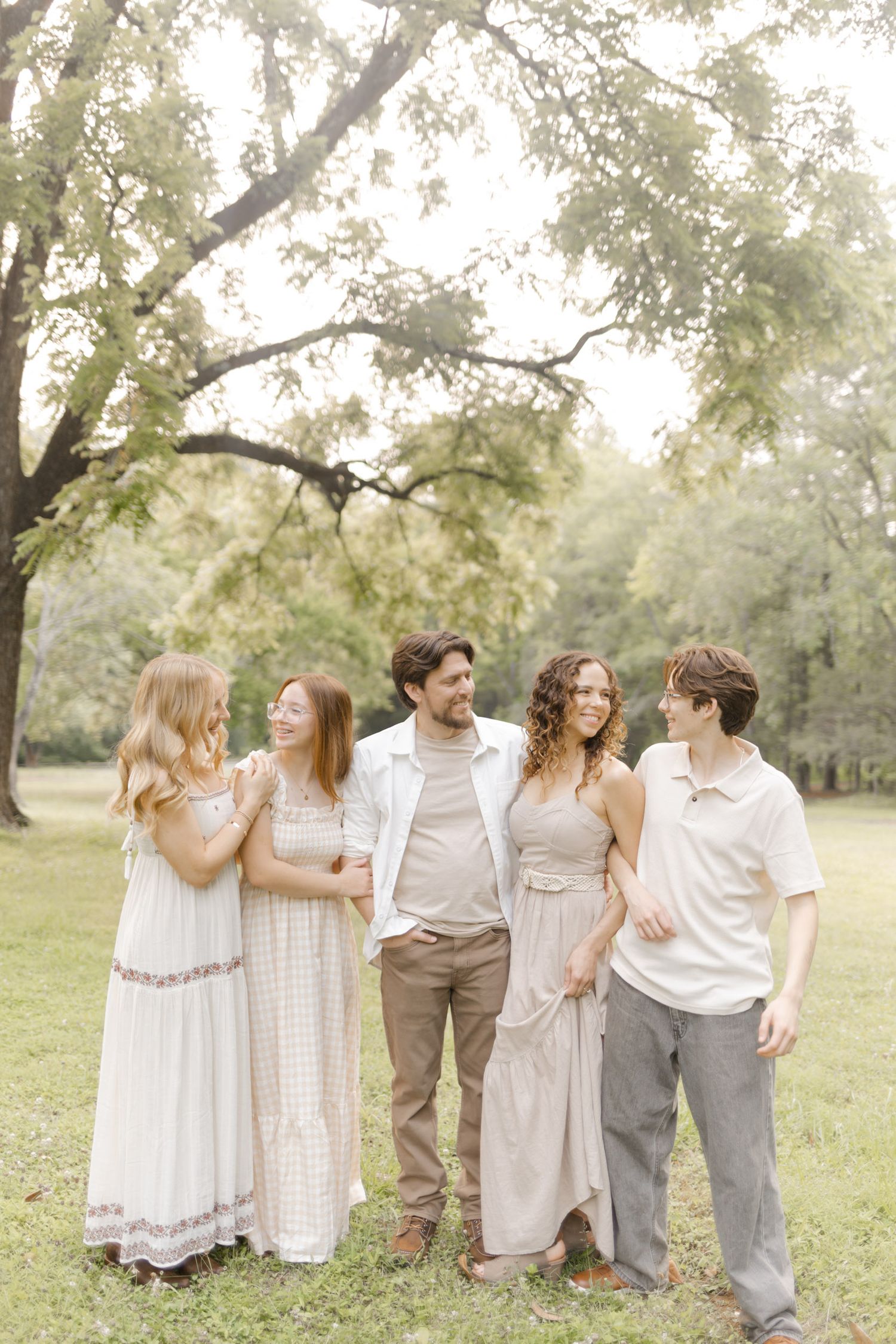 Friends gathered in casual elegant attire pose together under a large tree in a park setting during photoshoot with Kinsley Nicole Photo