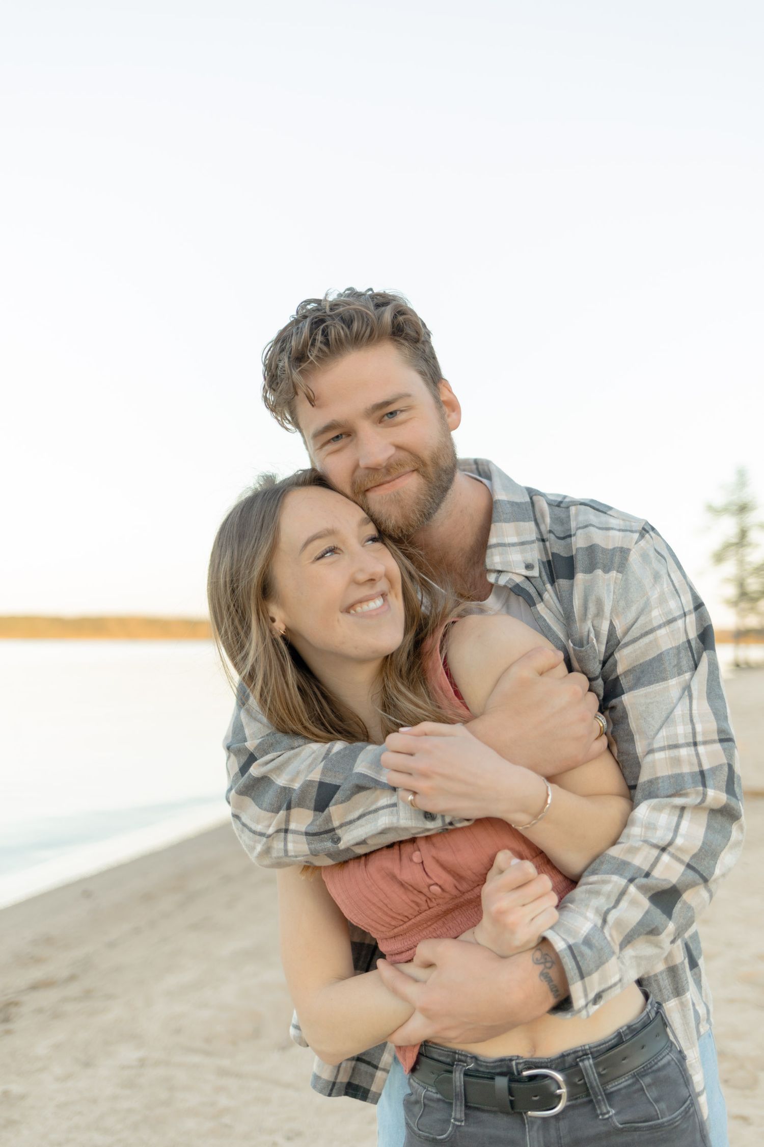 A warm embrace captured during golden hour on a beach with pine trees in the background during their couples lifestyle photoshoot in Raleigh