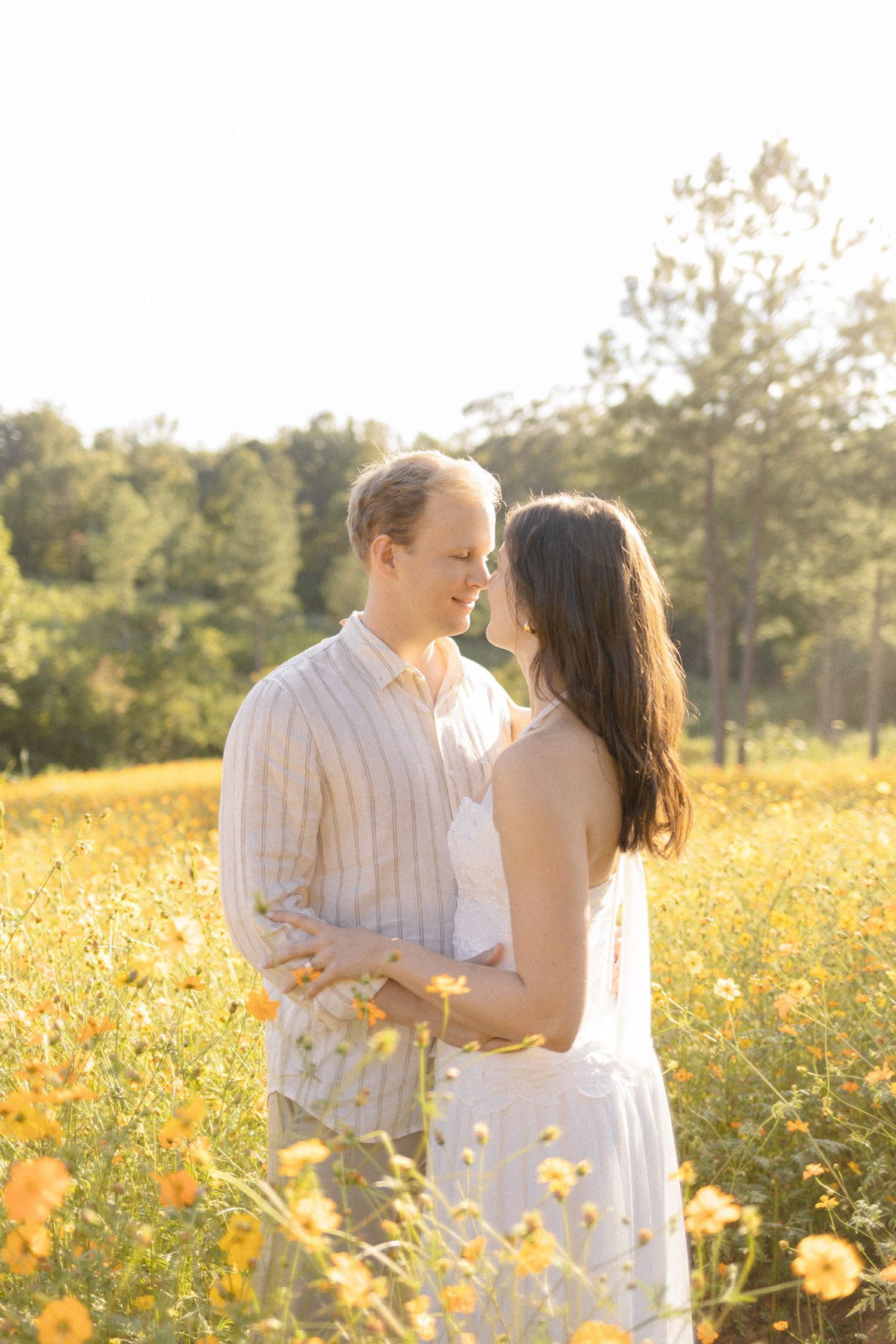 Romantic couple shares intimate moments in a field of yellow flowers during sunset for engagement photoshoot in Chapel Hill, NC.