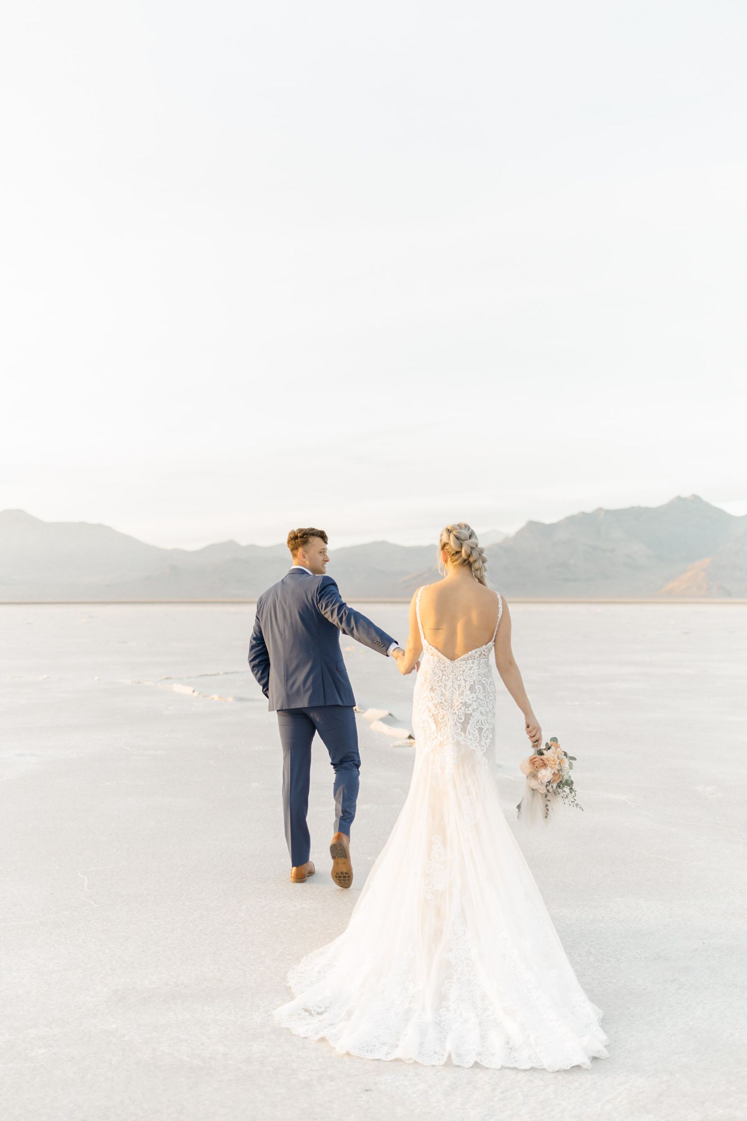 A couple in wedding attire strolls together on the pristine white salt flats during their desert elopement.