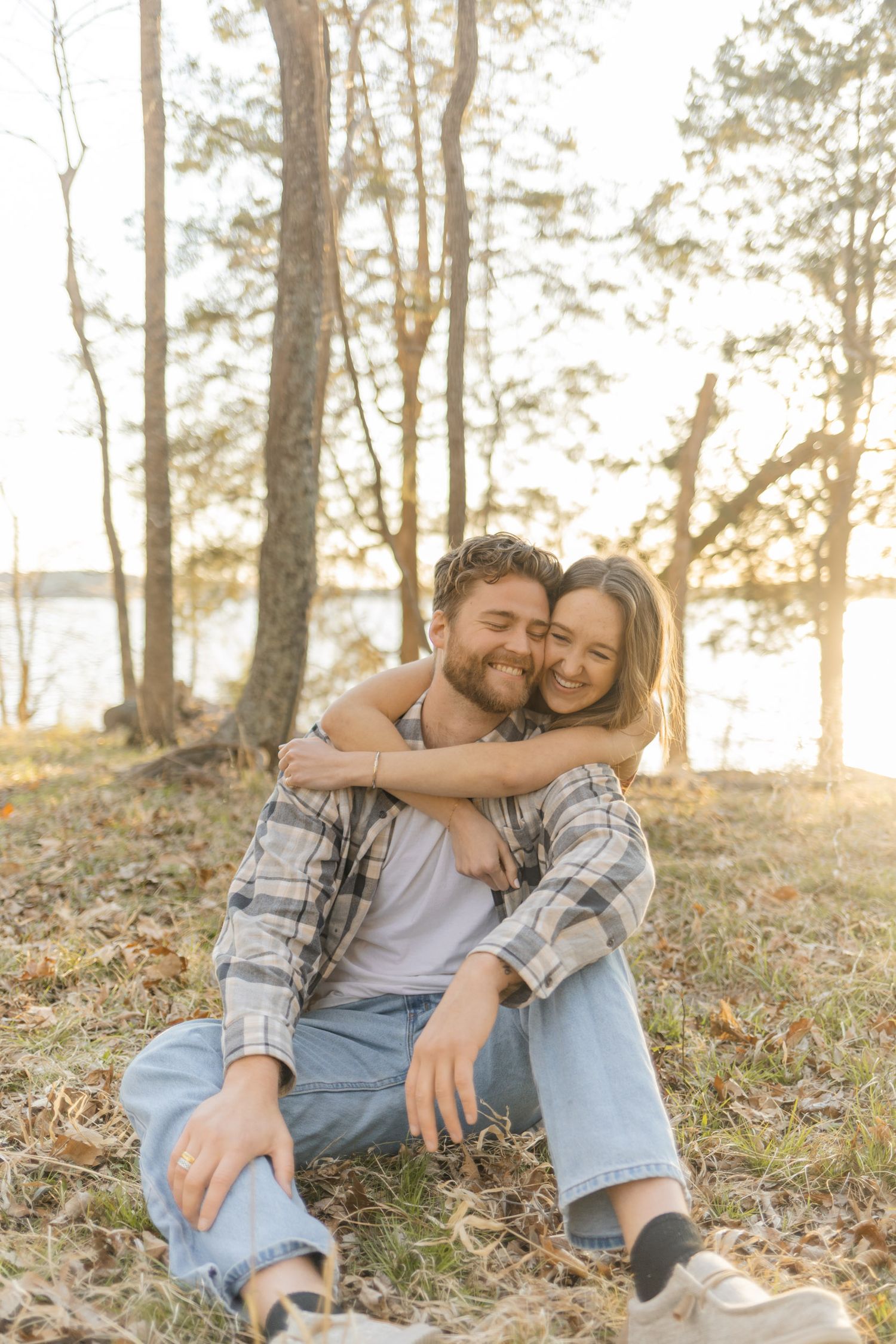 Couple sharing tender moment while resting on fallen leaves in sunlit forest in Raleigh, North Carolina.