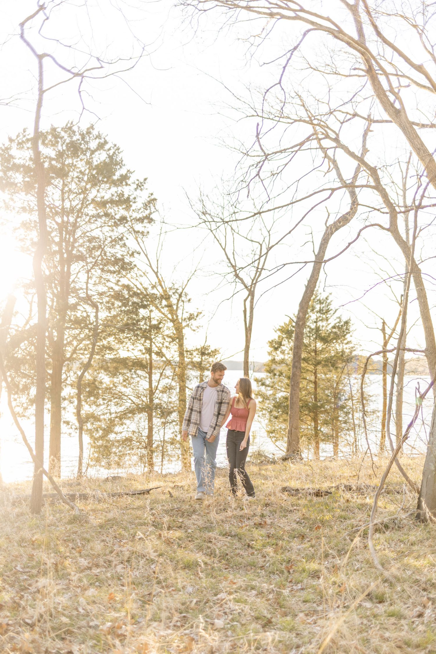 A couple shares a romantic moment in a sunlit wooded area during golden hour during photoshoot with Kinsley Nicole Photography.