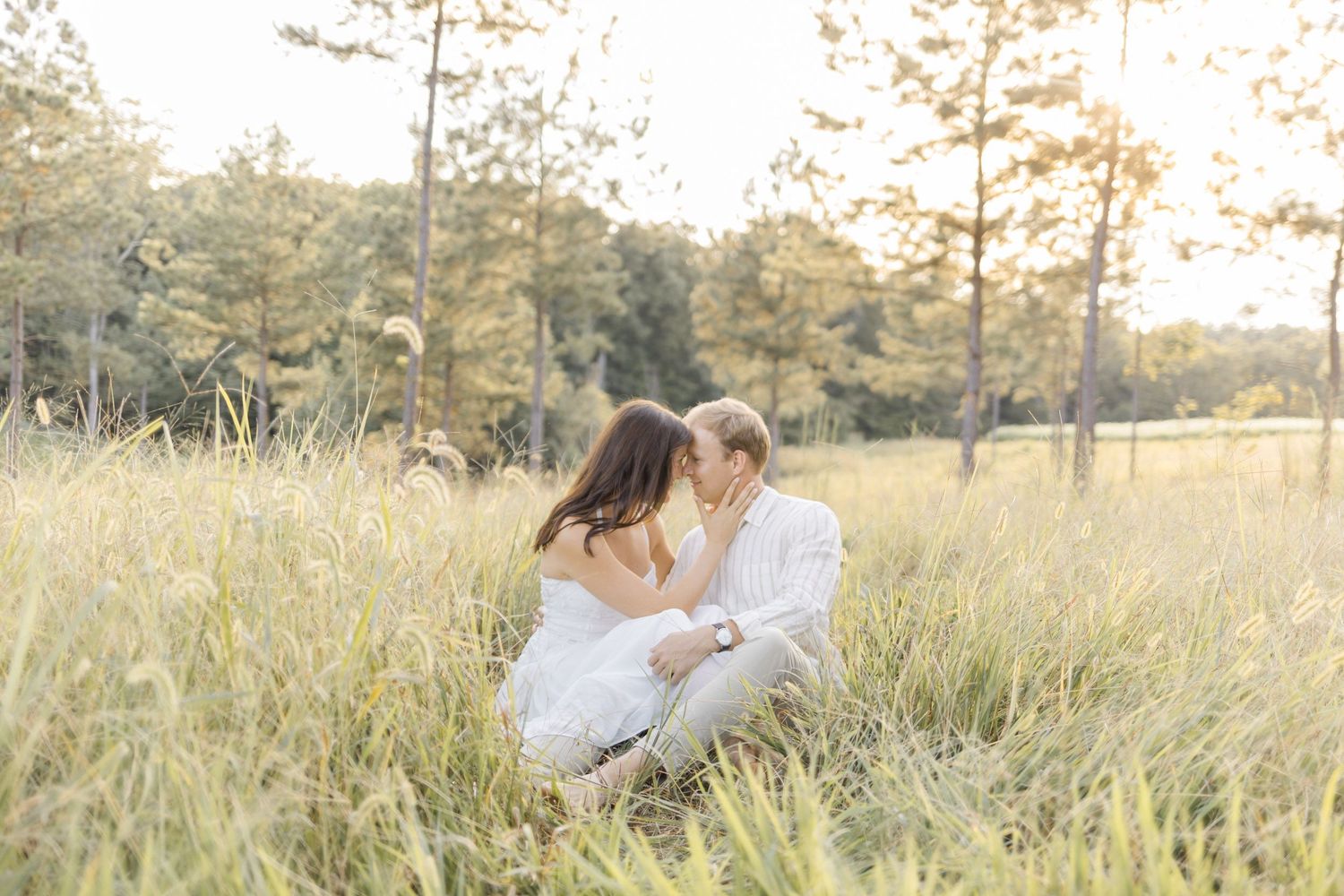 Romantic couple sharing intimate moments in a sun-kissed field with tall grass during lifestyle portrait photoshoot.