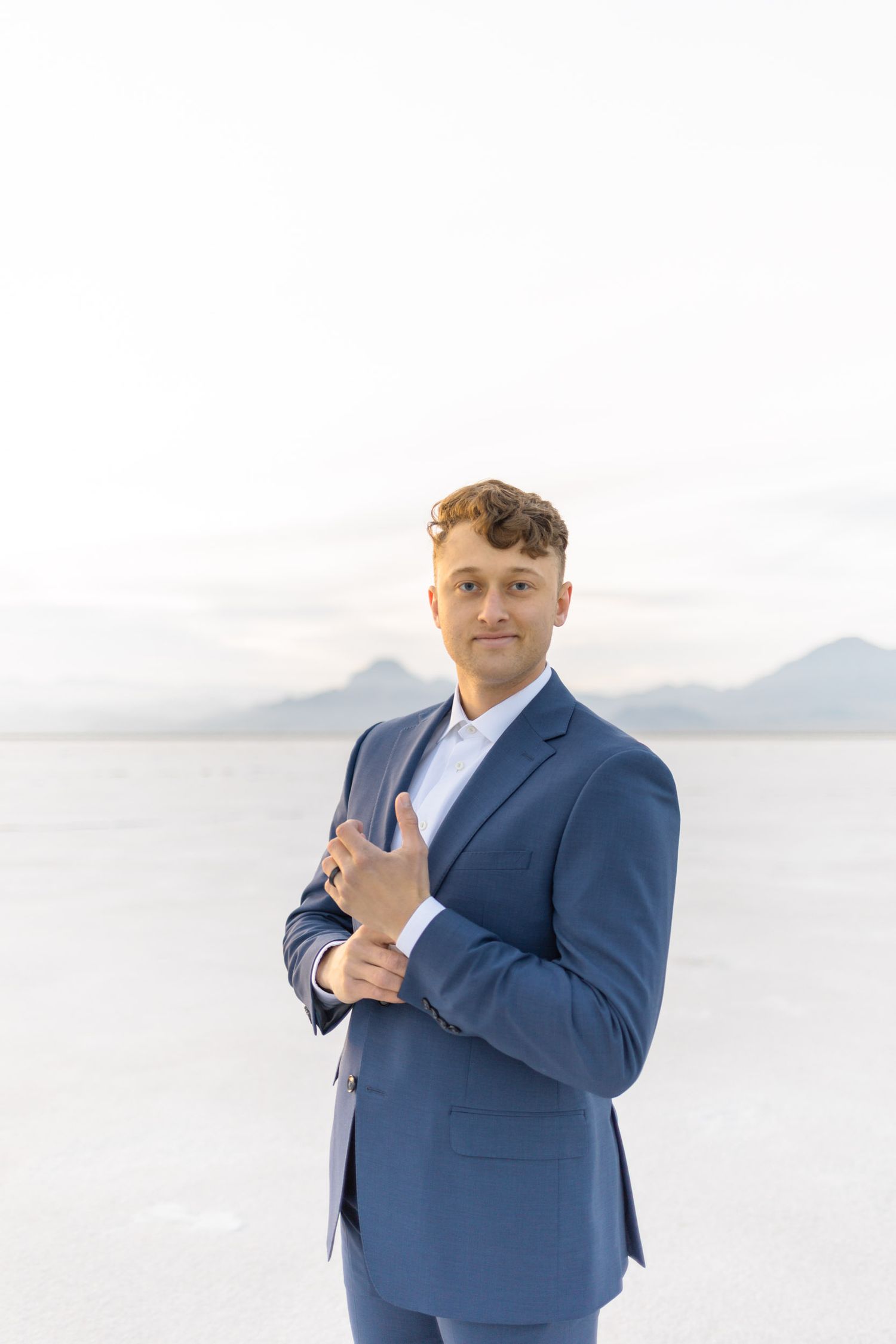 Groom in blue suit poses confidently against bright white background.