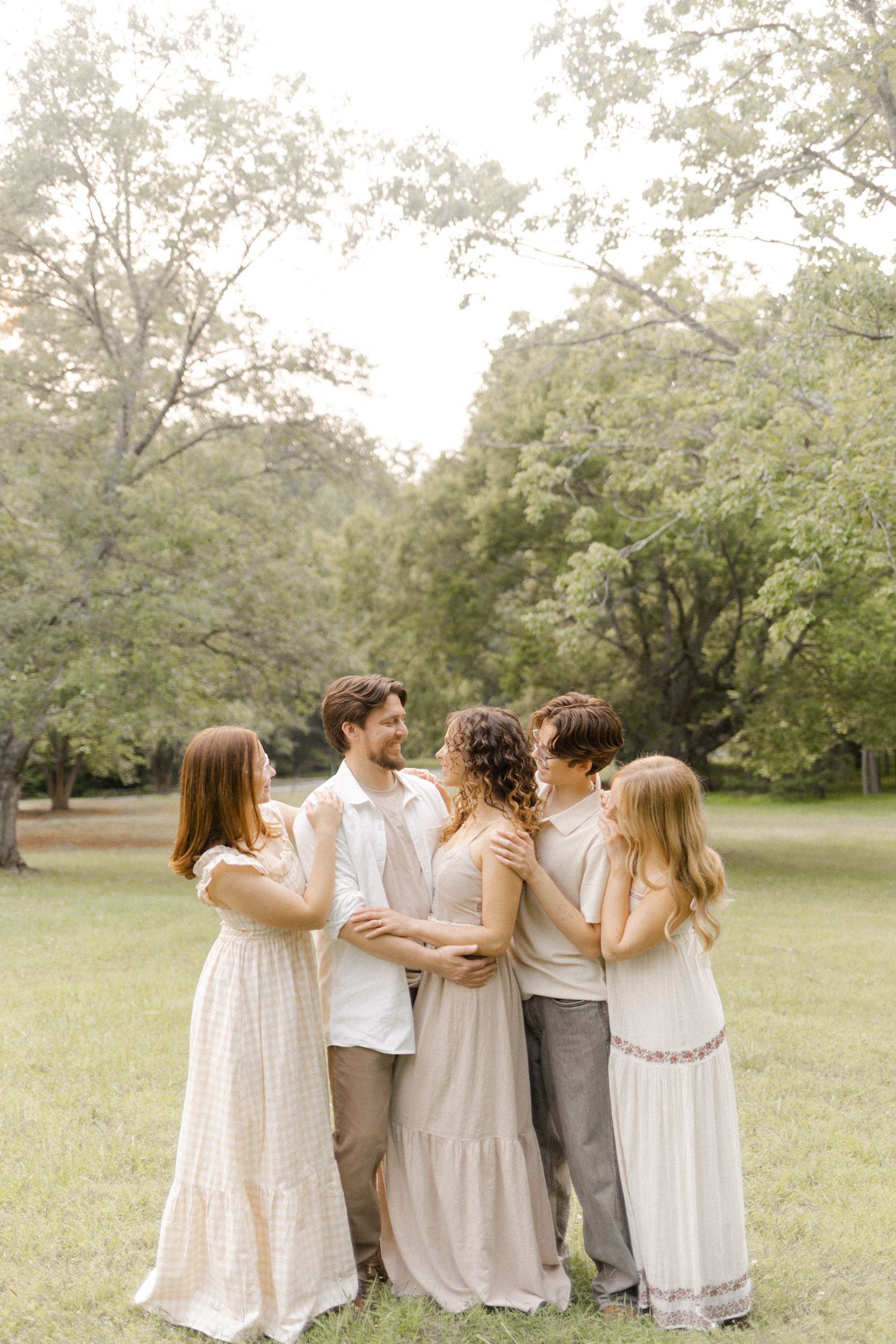 Group of people in white and neutral clothing embracing in a park setting in Durham, NC