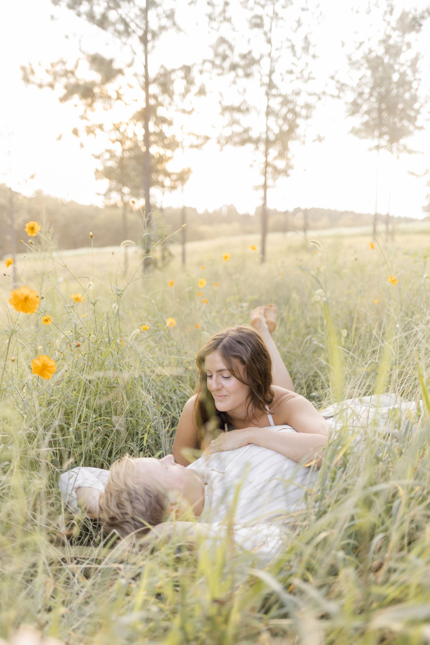 Couple lying in tall grass with orange wildflowers during a golden sunset during engagement session with photographer in North Carolina.