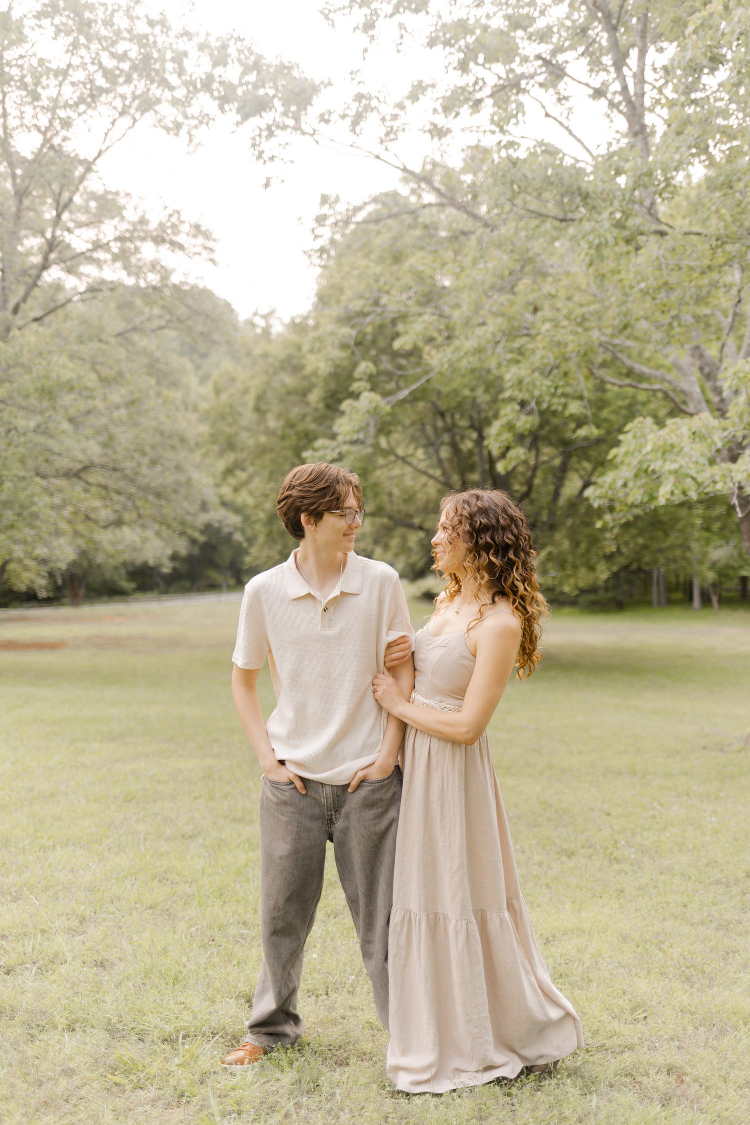 Two people share a playful moment together in a sunlit meadow with trees in the background with Durham, North Carolina Photographer.