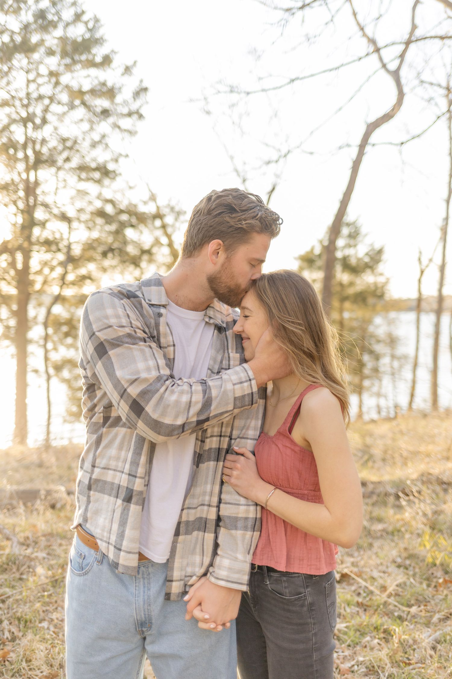 Romantic couple embracing in a forest setting with soft golden sunlight filtering through trees during photoshoot with Kinsley Nicole Photo